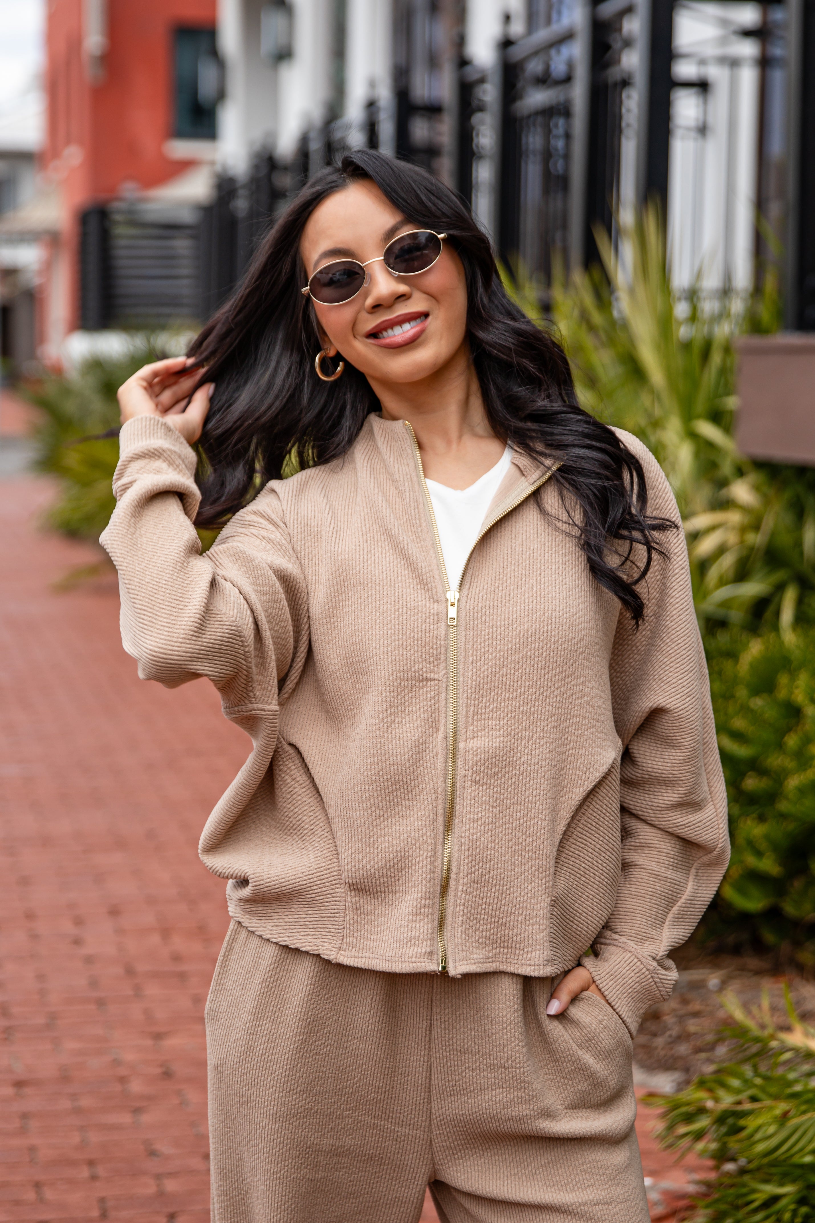 Woman wearing a beige zip-up jacket and pants outdoors.