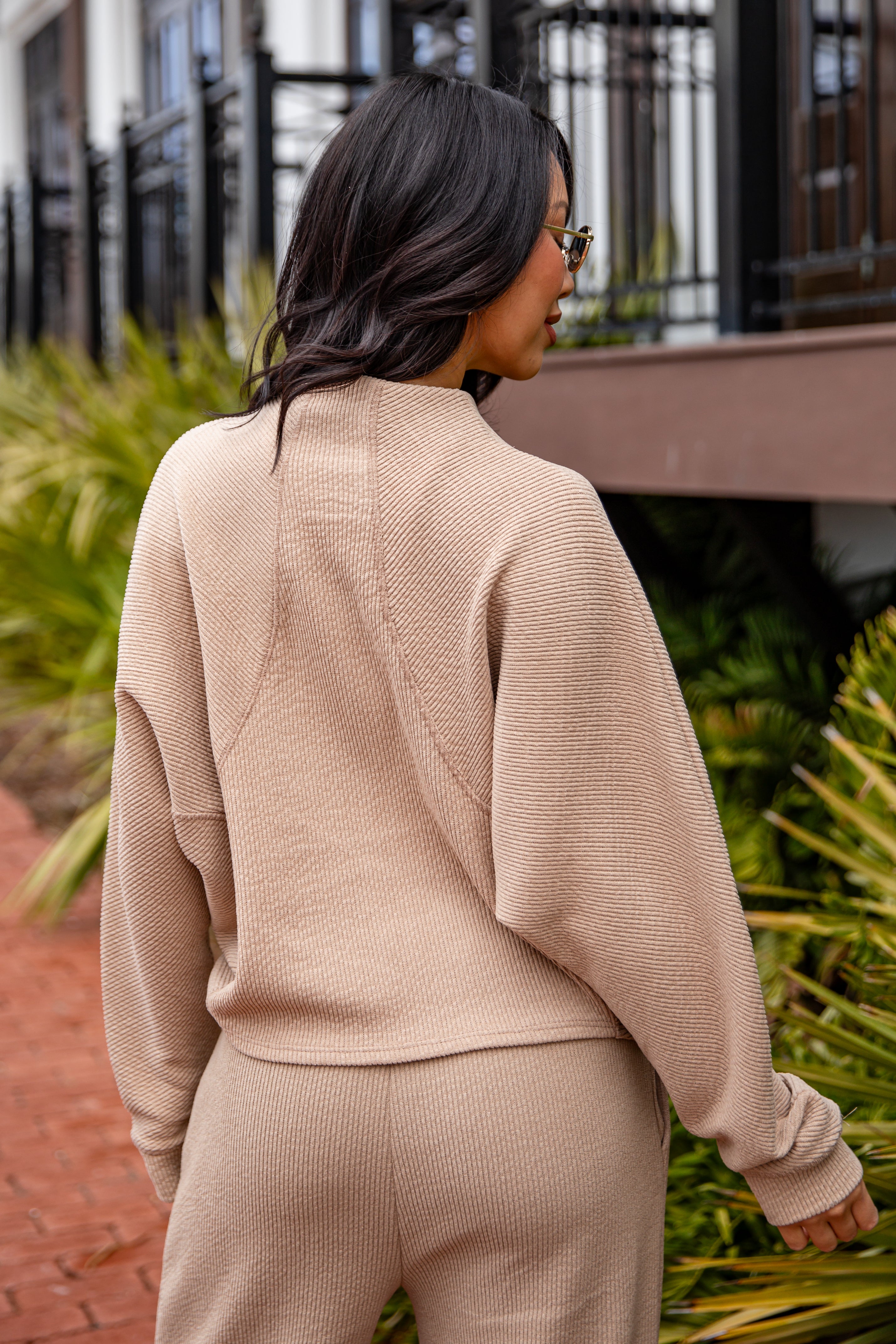 Woman wearing a beige outfit standing outdoors with plants and a building in the background