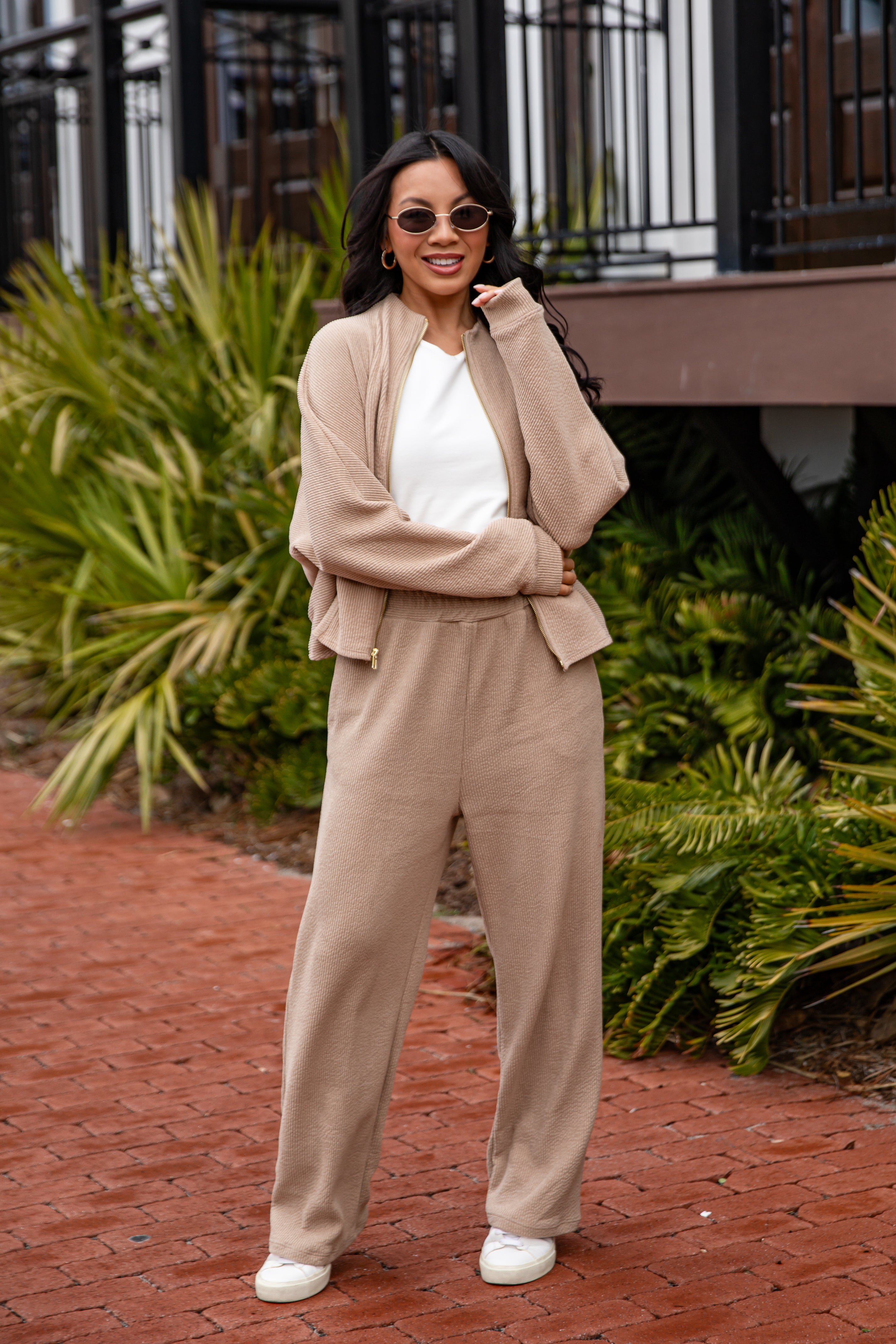 Woman in beige outfit standing outdoors with greenery in the background