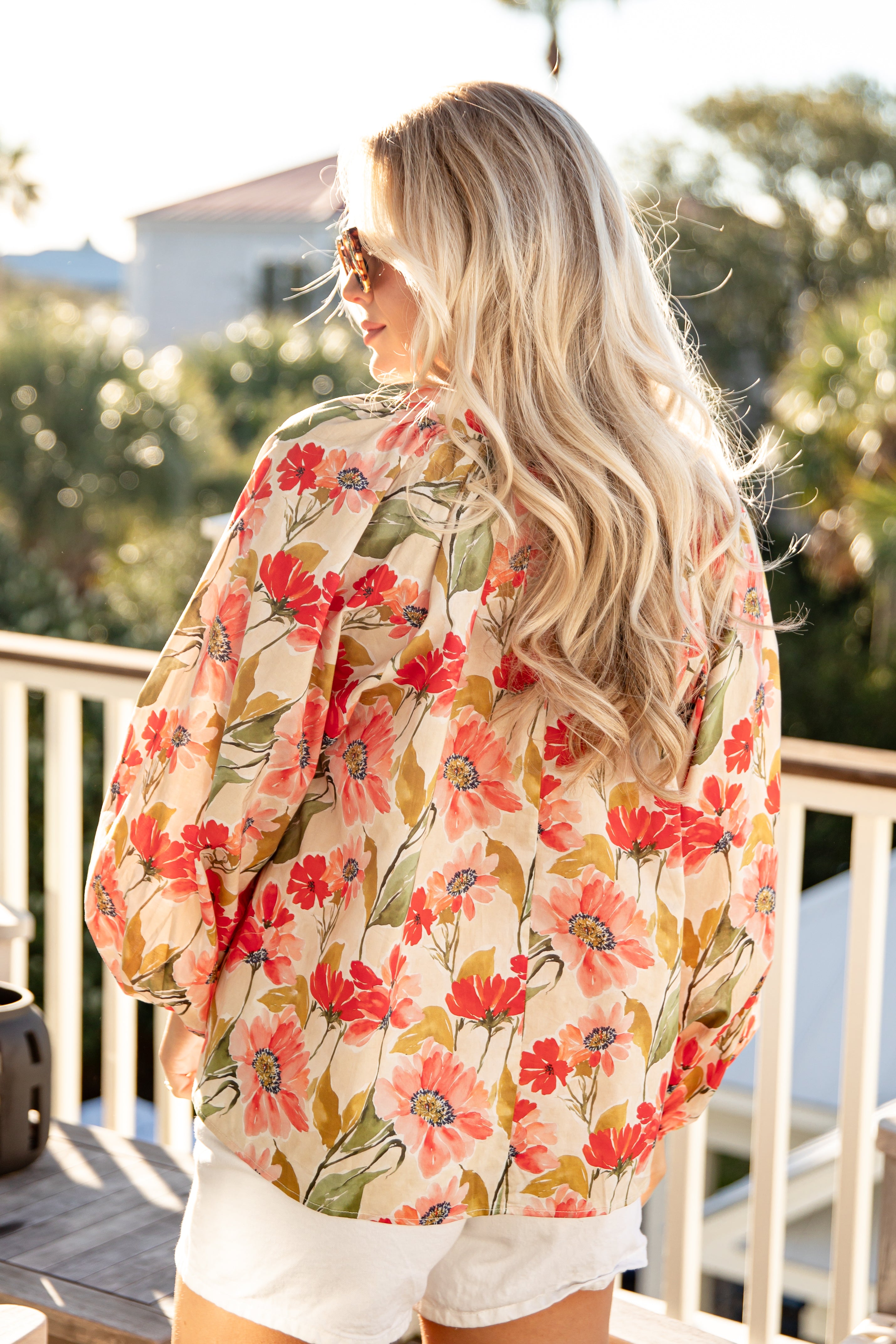 Woman wearing a floral kimono-style garment on a balcony with greenery in the background