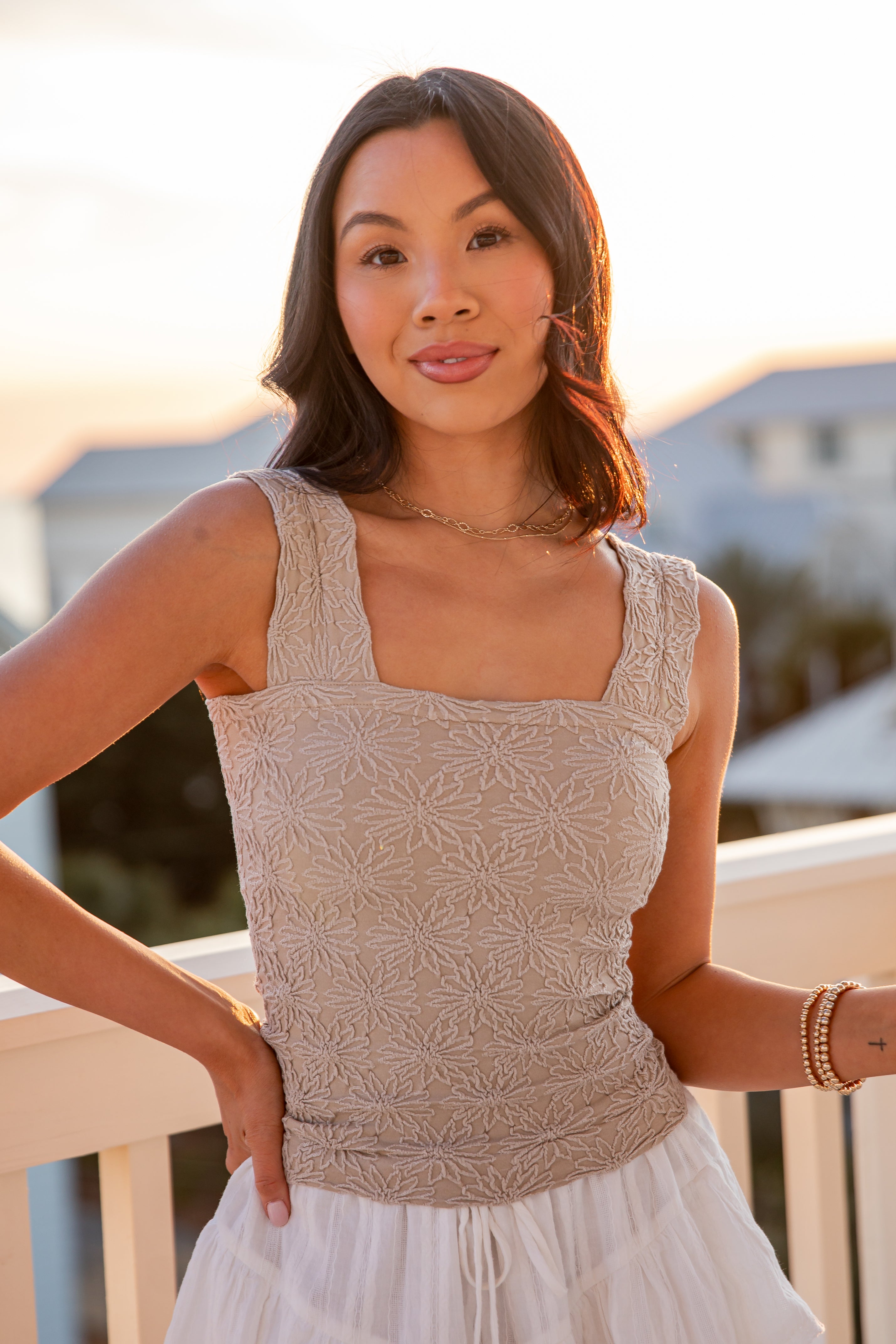 Woman wearing a beige sleeveless top and white skirt on a balcony.