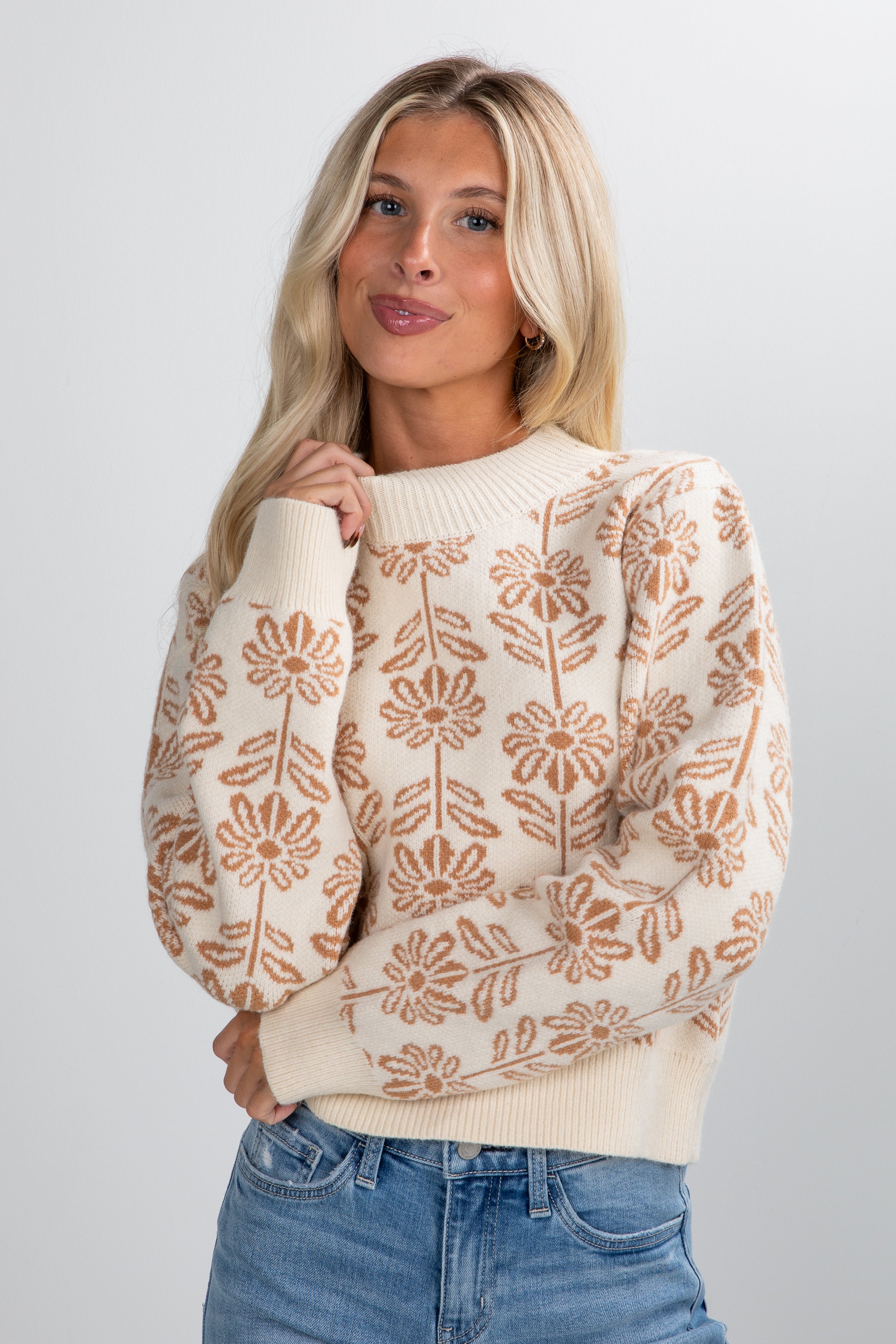 Woman wearing a beige sweater with floral patterns on a plain background