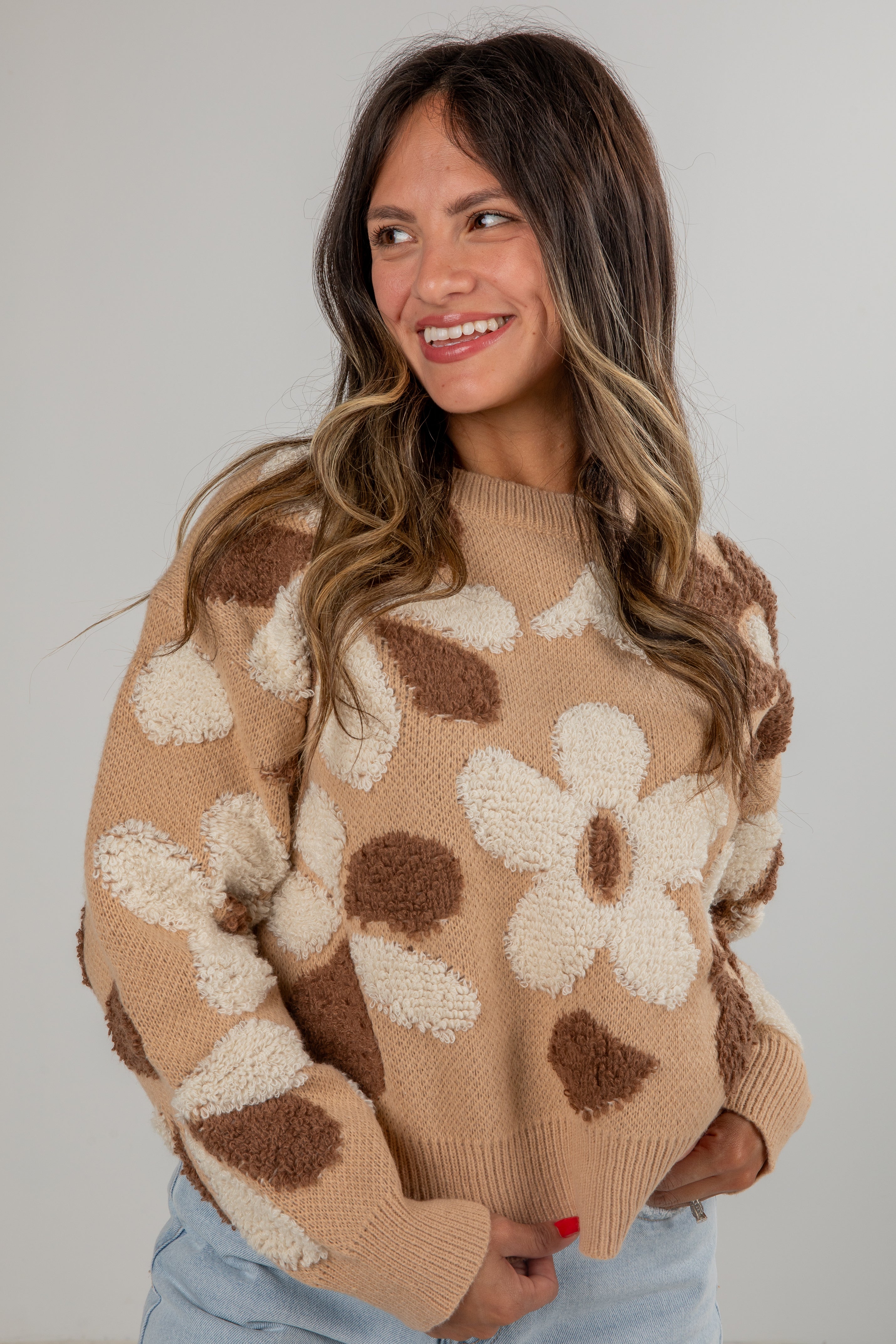 Woman wearing a beige sweater with brown and white floral patterns against a plain background