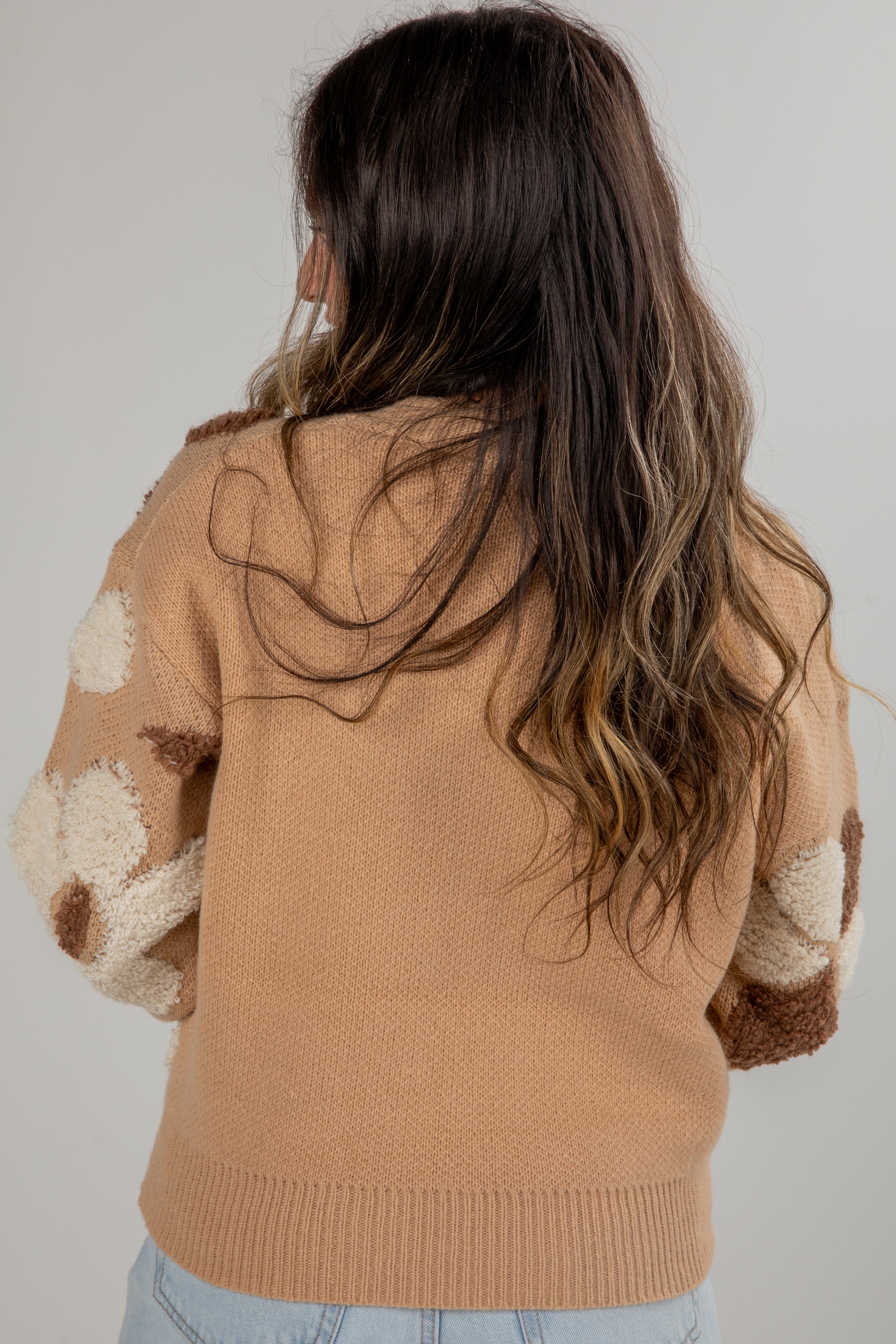 Person wearing a brown sweater with patterned sleeves on a plain background