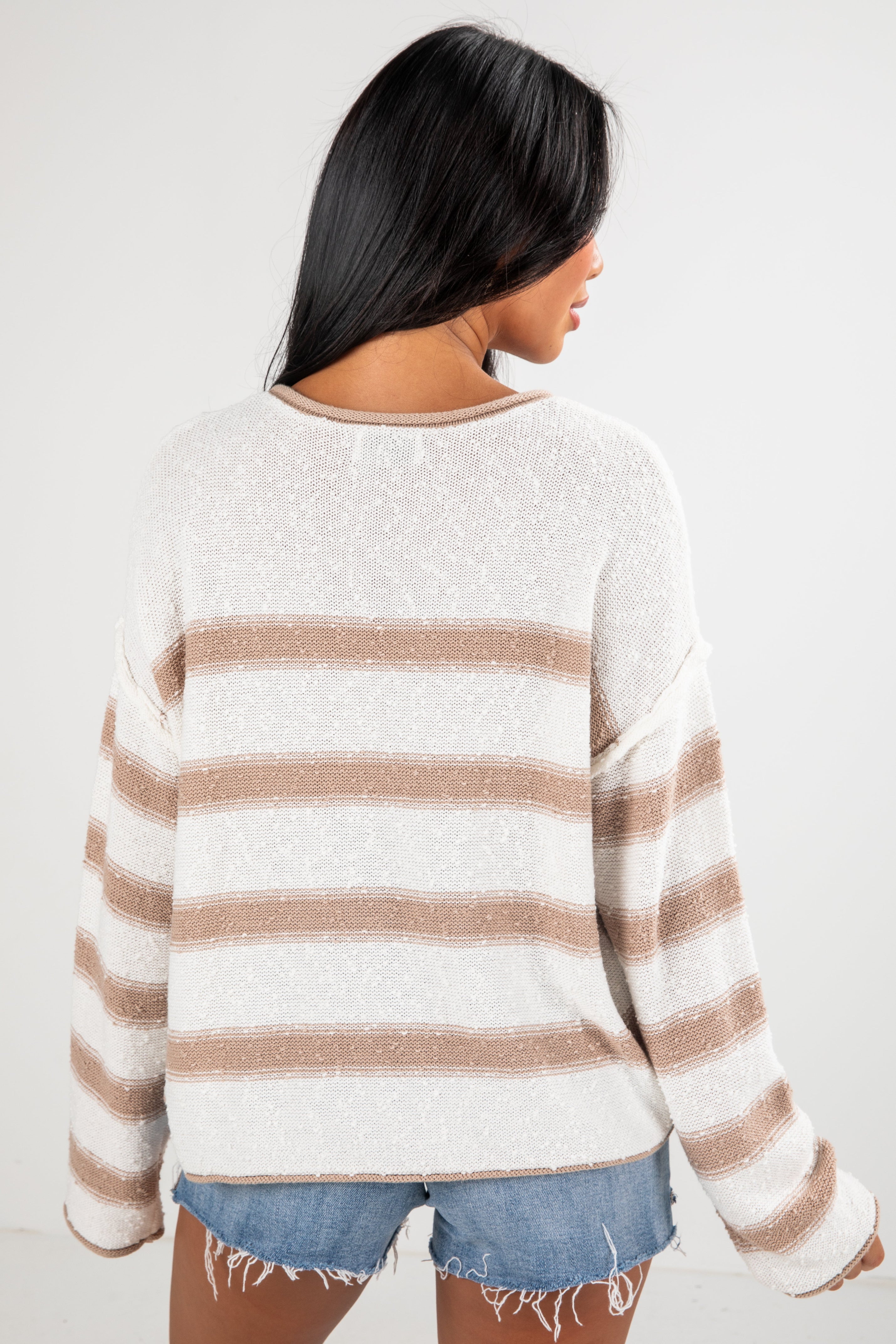 Person wearing a white and brown striped sweater with denim shorts on a plain background