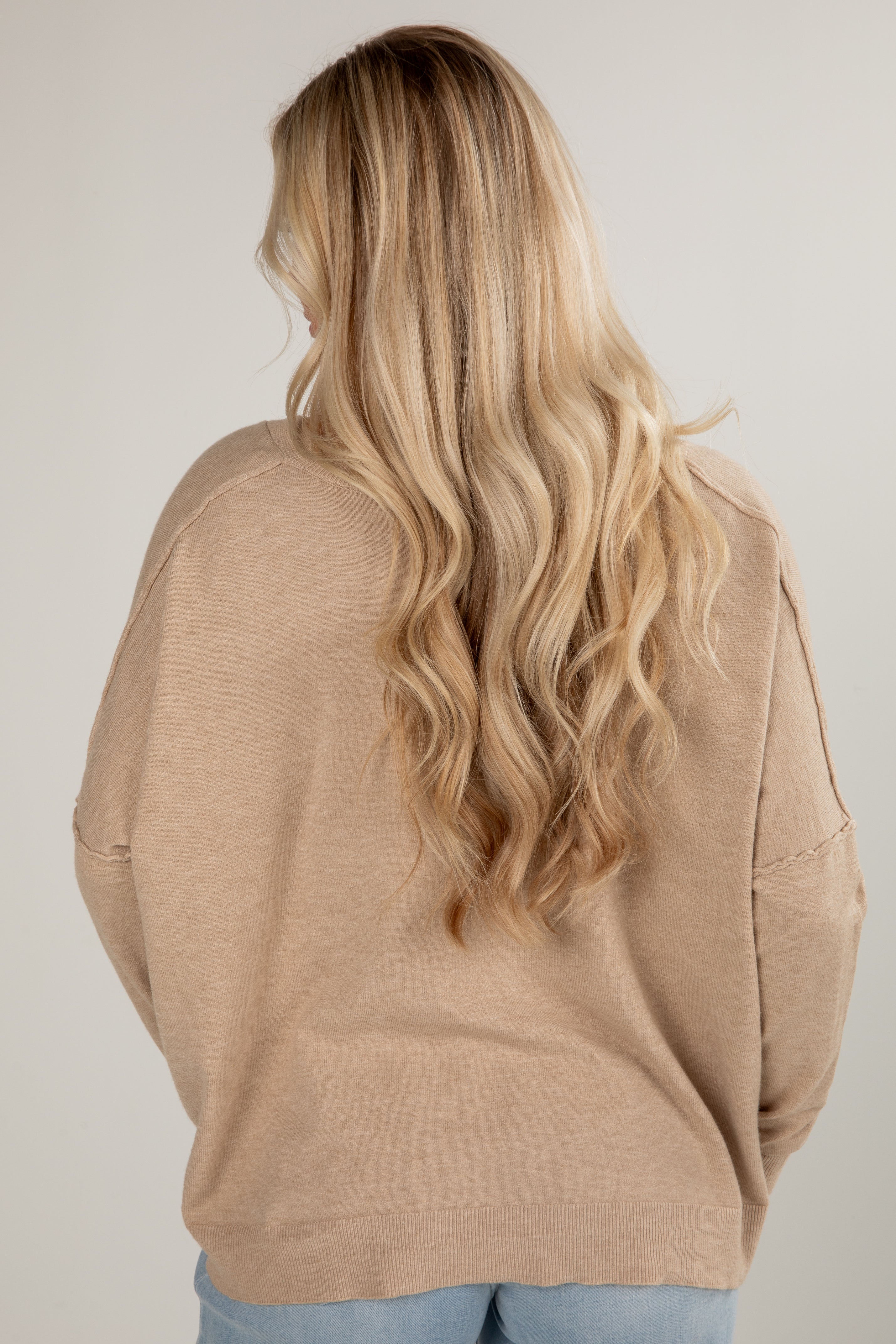 Person wearing a beige sweater with long blonde hair on a plain background