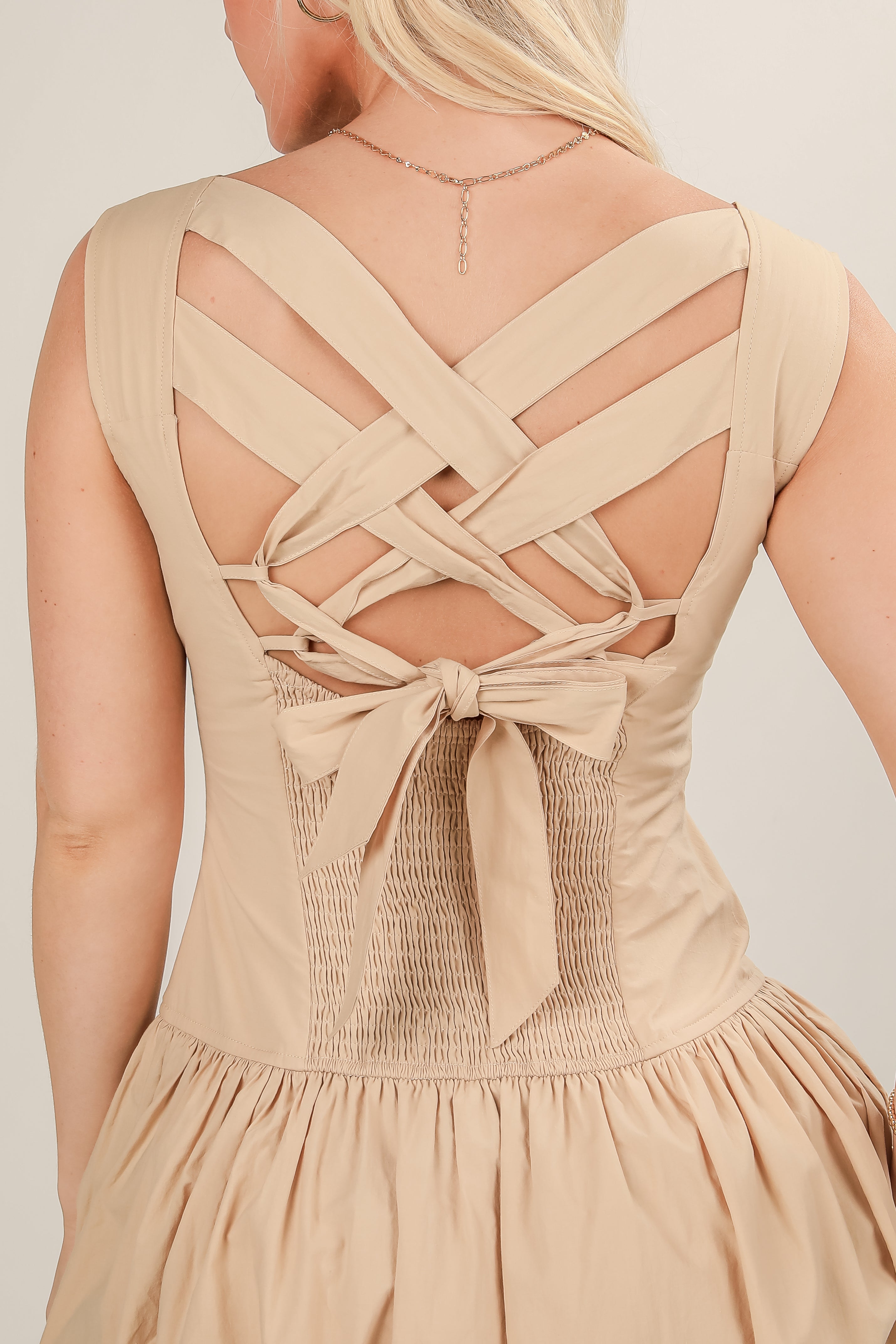 Beige dress with criss-cross back design on a plain background