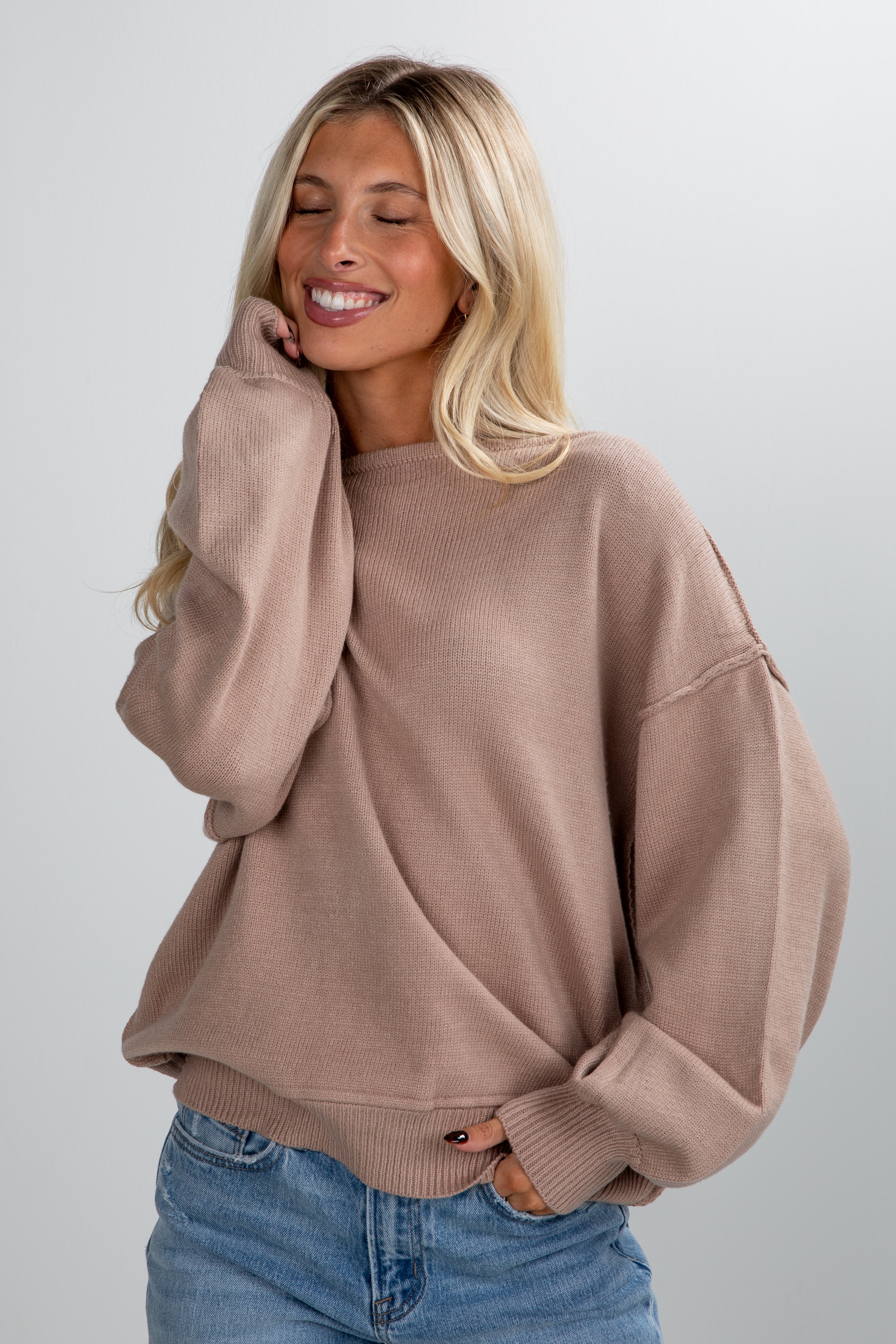 Woman wearing a brown sweater and blue jeans against a plain background