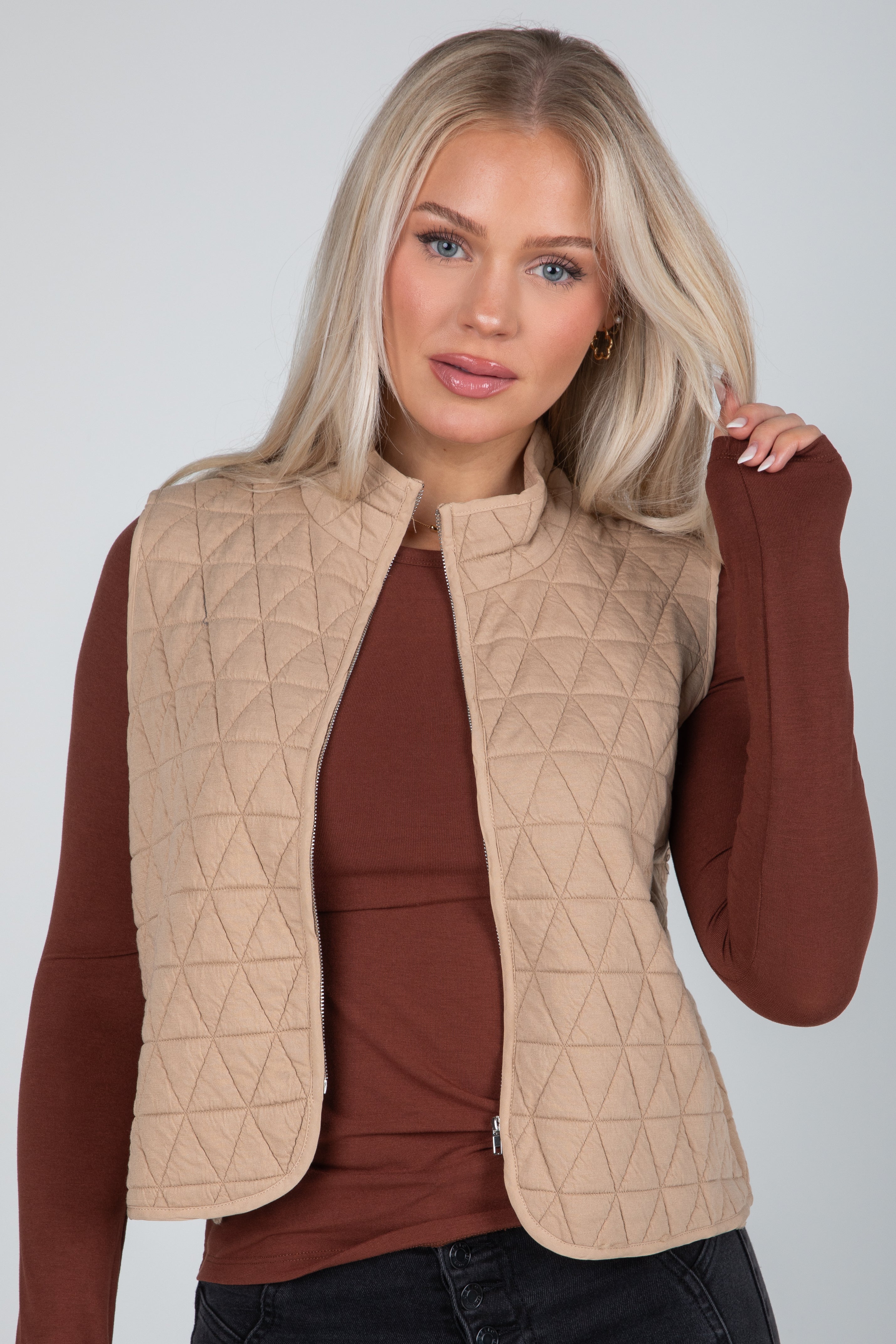 Woman wearing a beige quilted vest over a brown long-sleeve shirt on a plain background