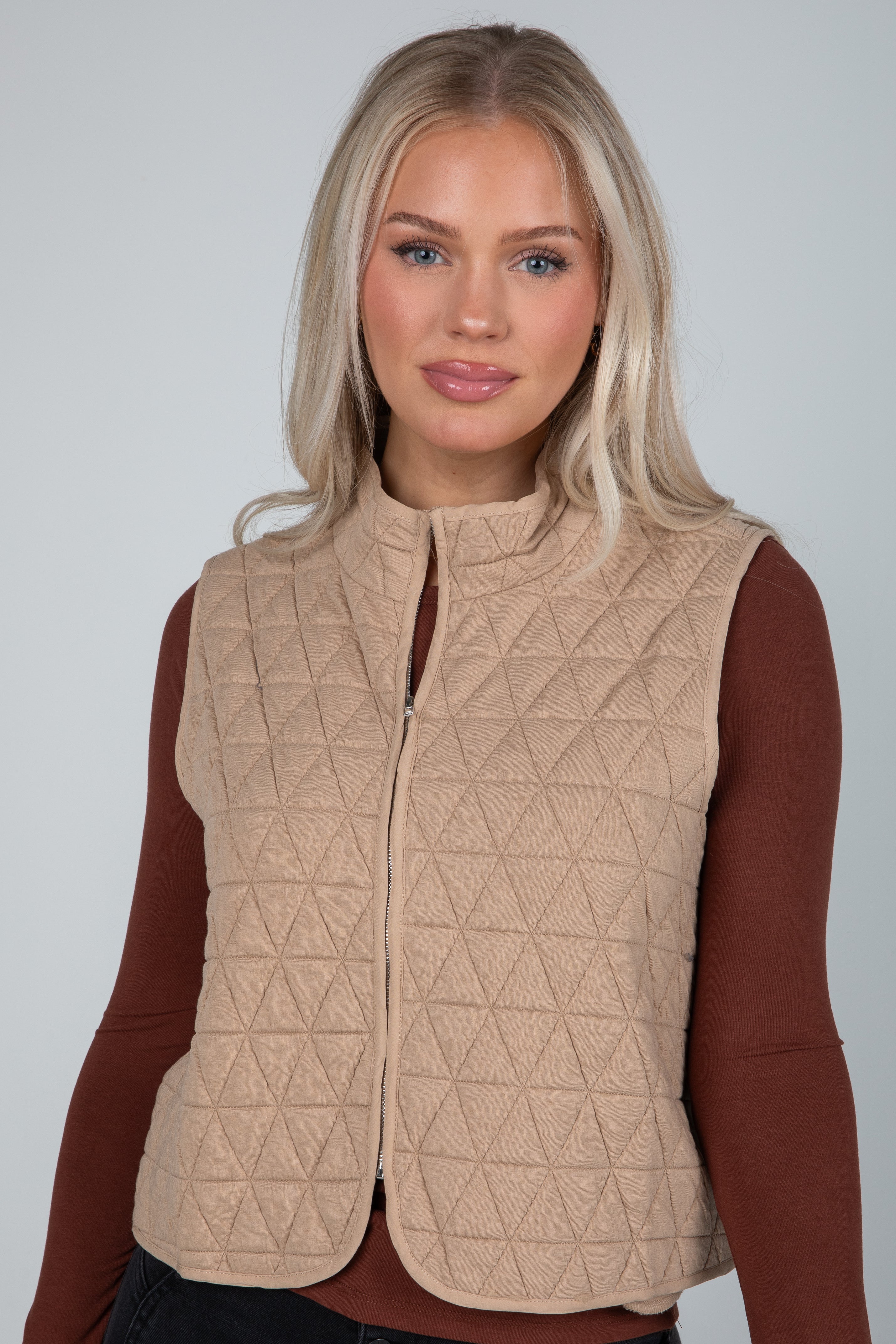 Woman wearing a beige quilted vest against a plain background