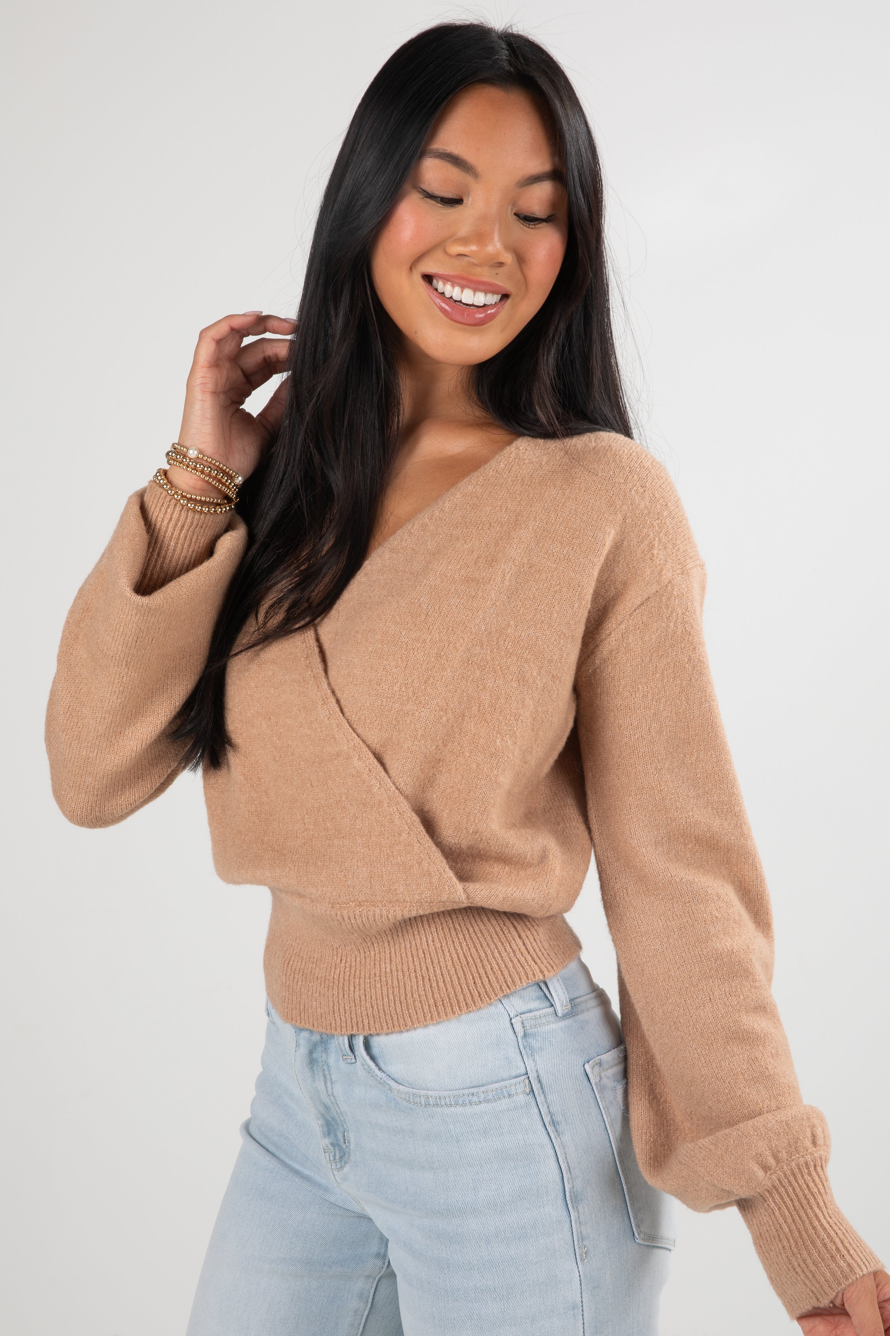 Woman wearing a beige sweater and light blue jeans against a white background