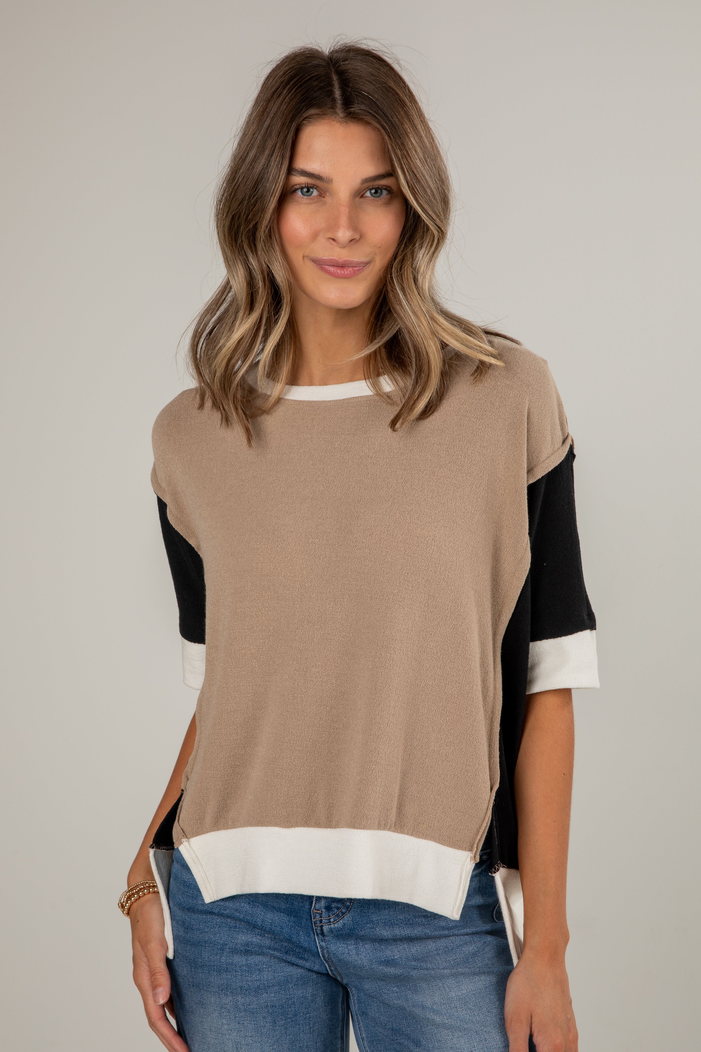 Woman wearing a beige and black color-blocked top with blue jeans on a plain background