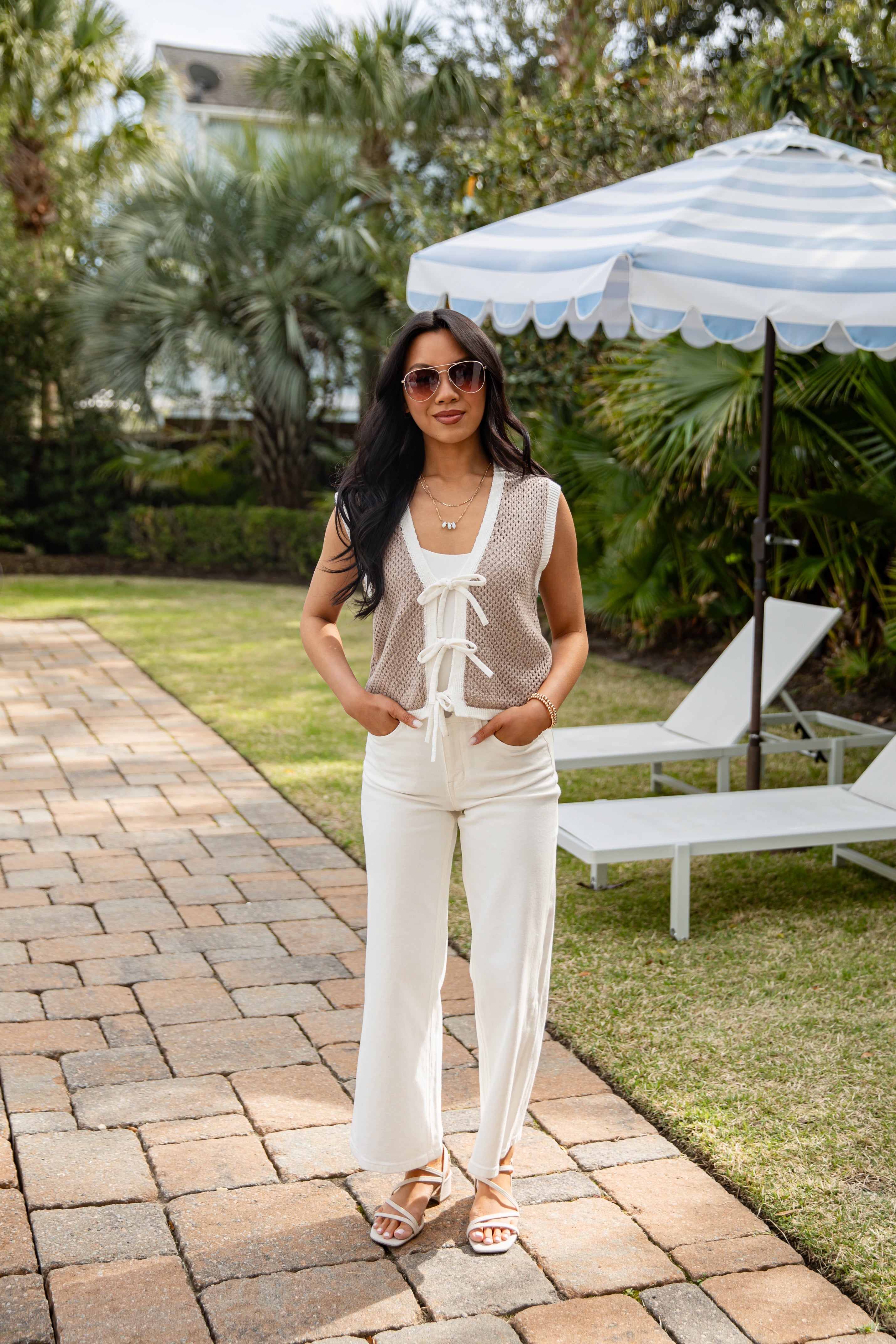Woman in a white outfit standing on a patio with outdoor furniture and greenery in the background