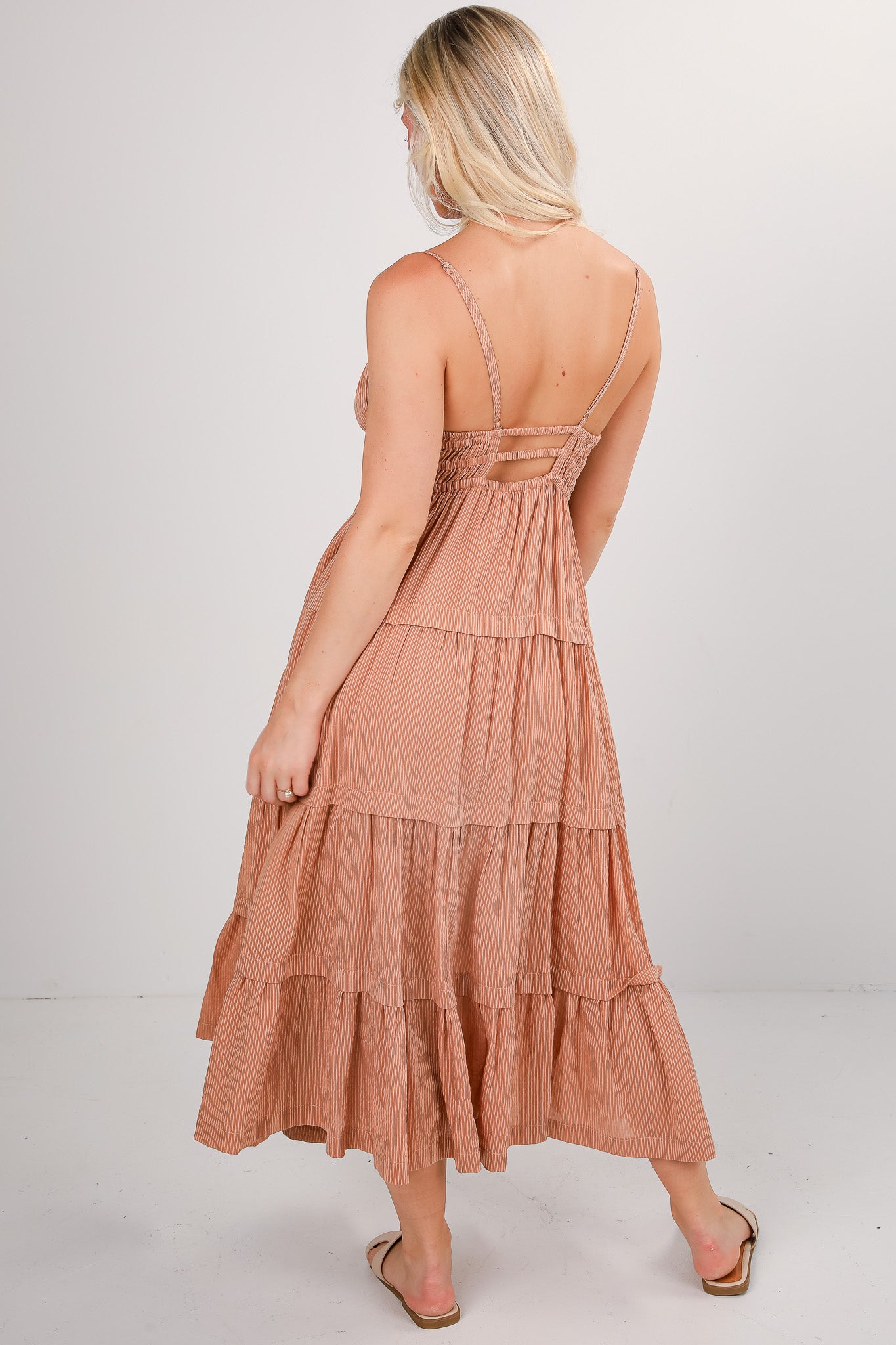 Woman wearing a tiered, sleeveless dress with thin straps on a white background