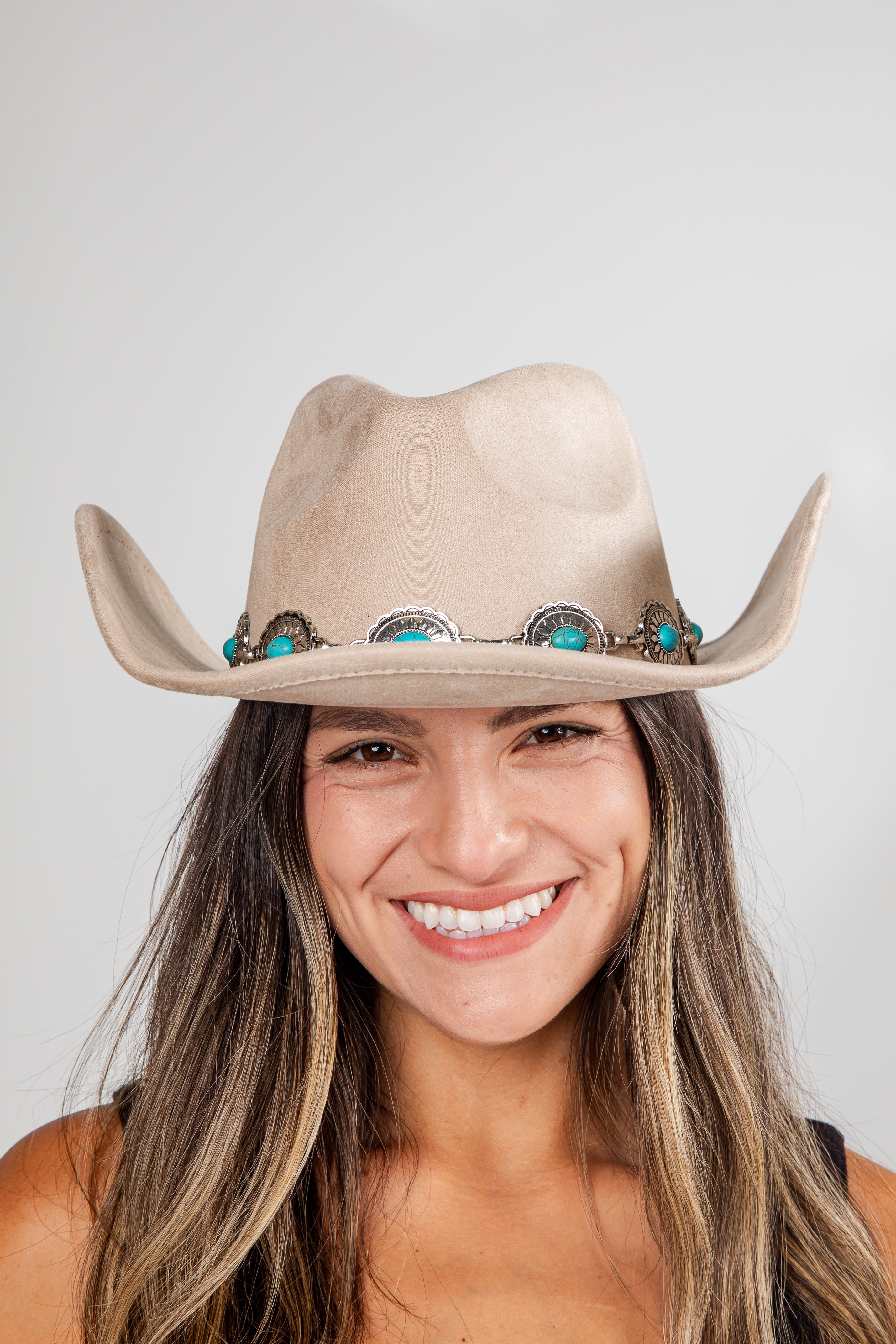 Woman wearing a beige cowboy hat with turquoise stones on a plain background