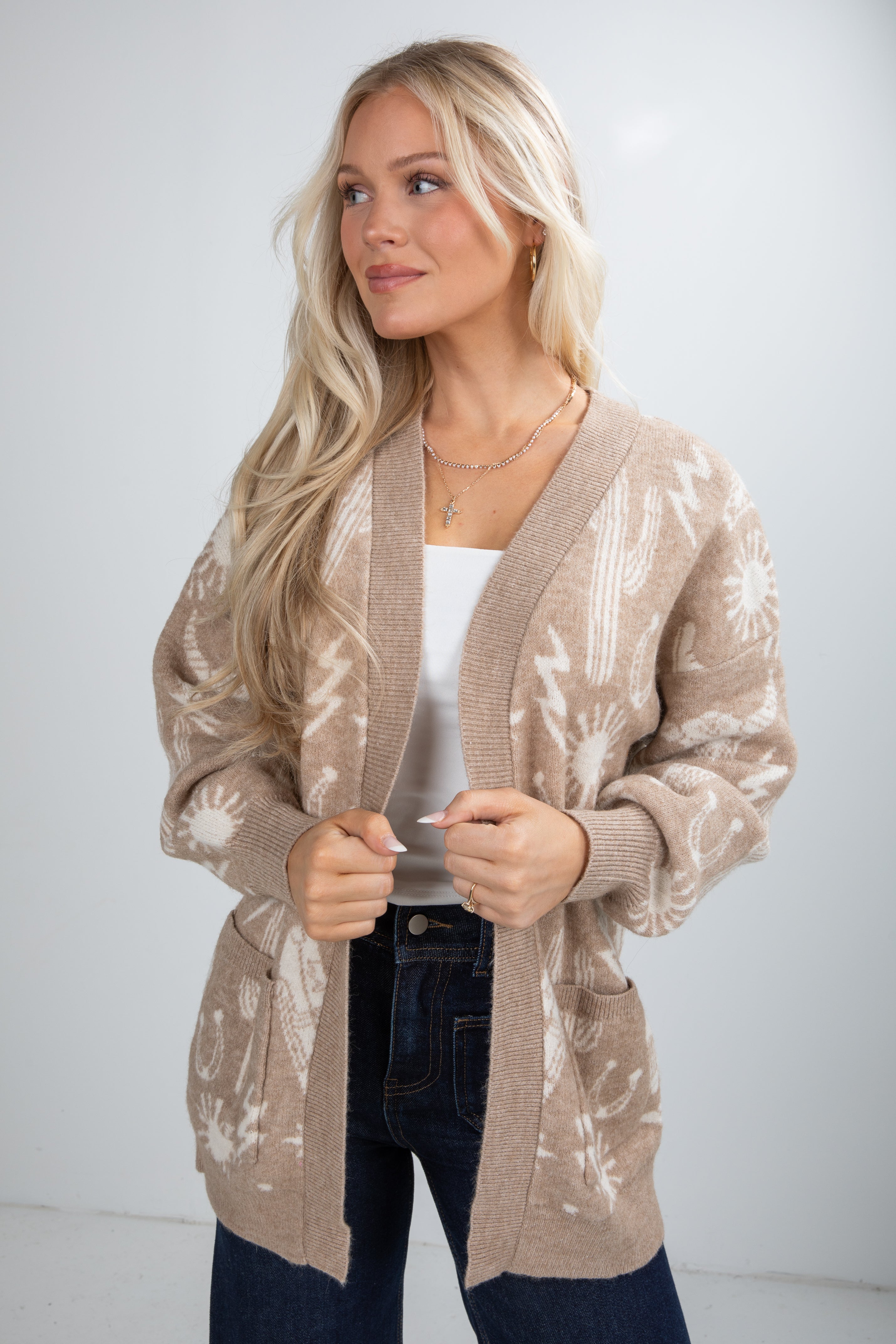 Woman wearing a beige patterned cardigan over a white top and dark jeans on a white background