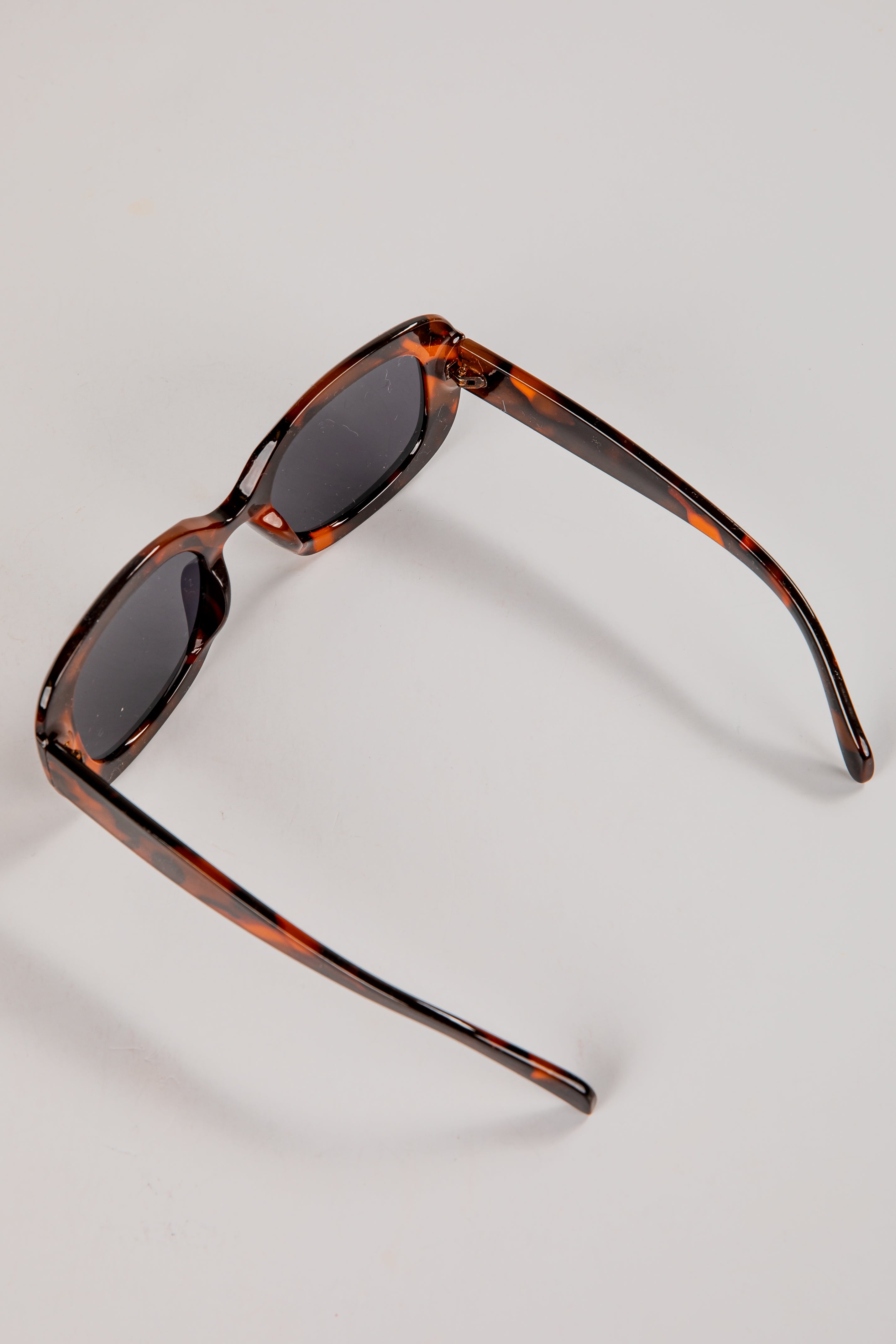 Sunglasses with tortoiseshell frame and dark lenses on a light gray background