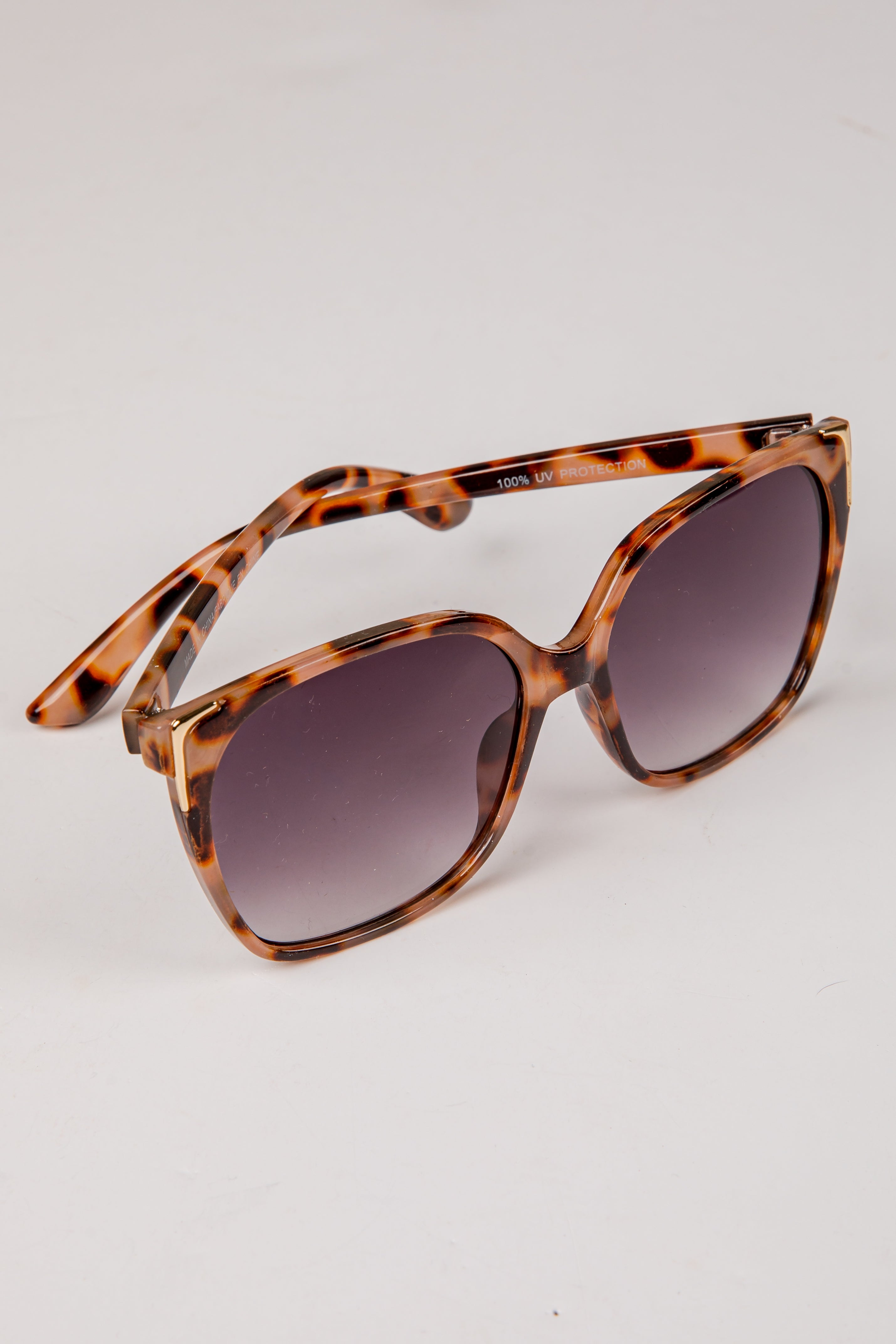 Sunglasses with tortoiseshell frame and dark lenses on a light gray background