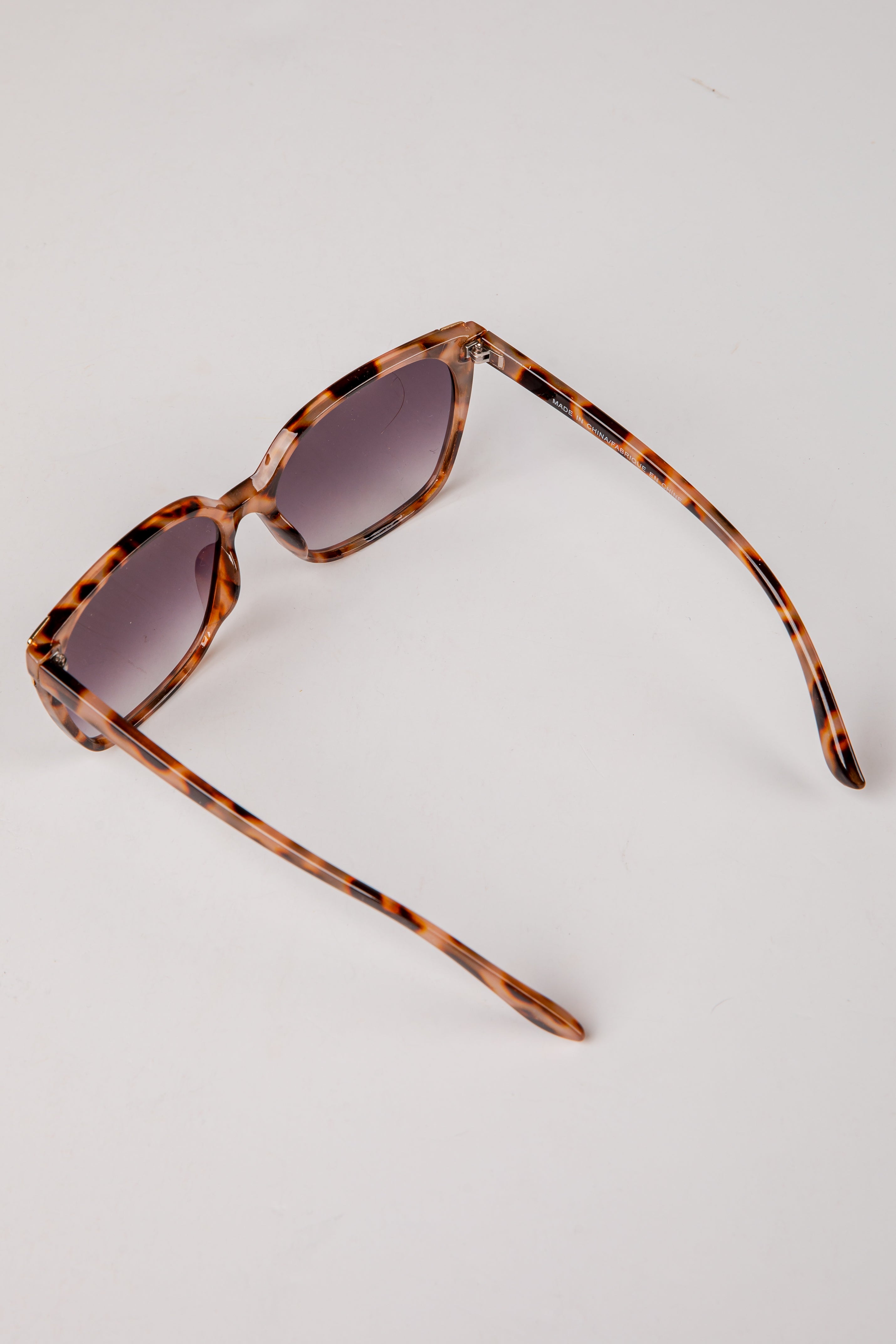 Sunglasses with tortoiseshell frame and dark lenses on a light gray background