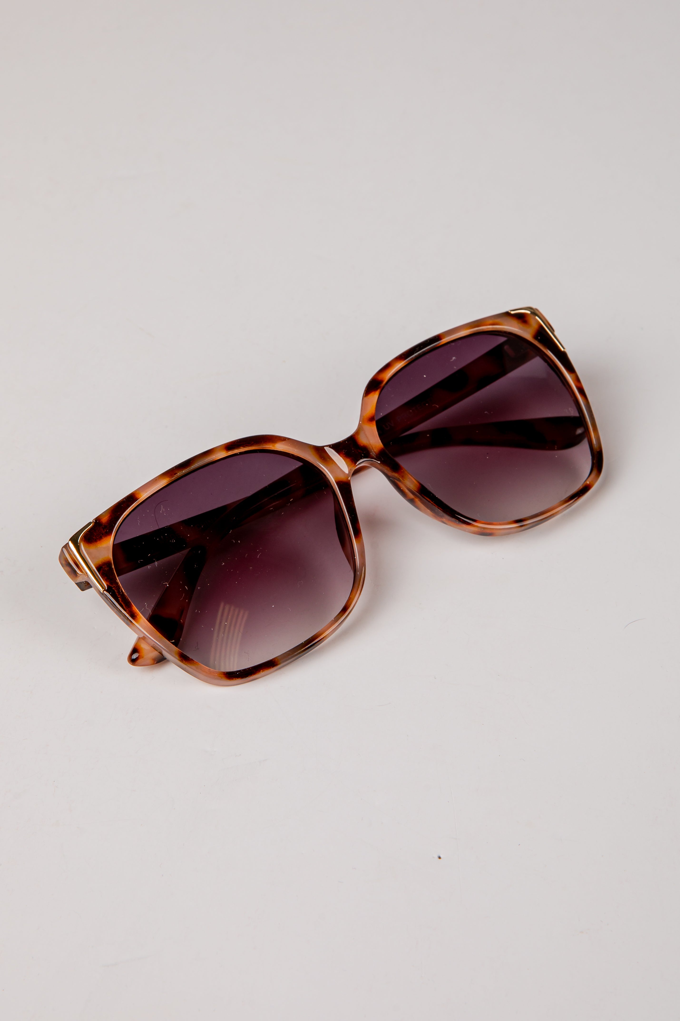 Sunglasses with tortoiseshell frame and dark lenses on a light gray background