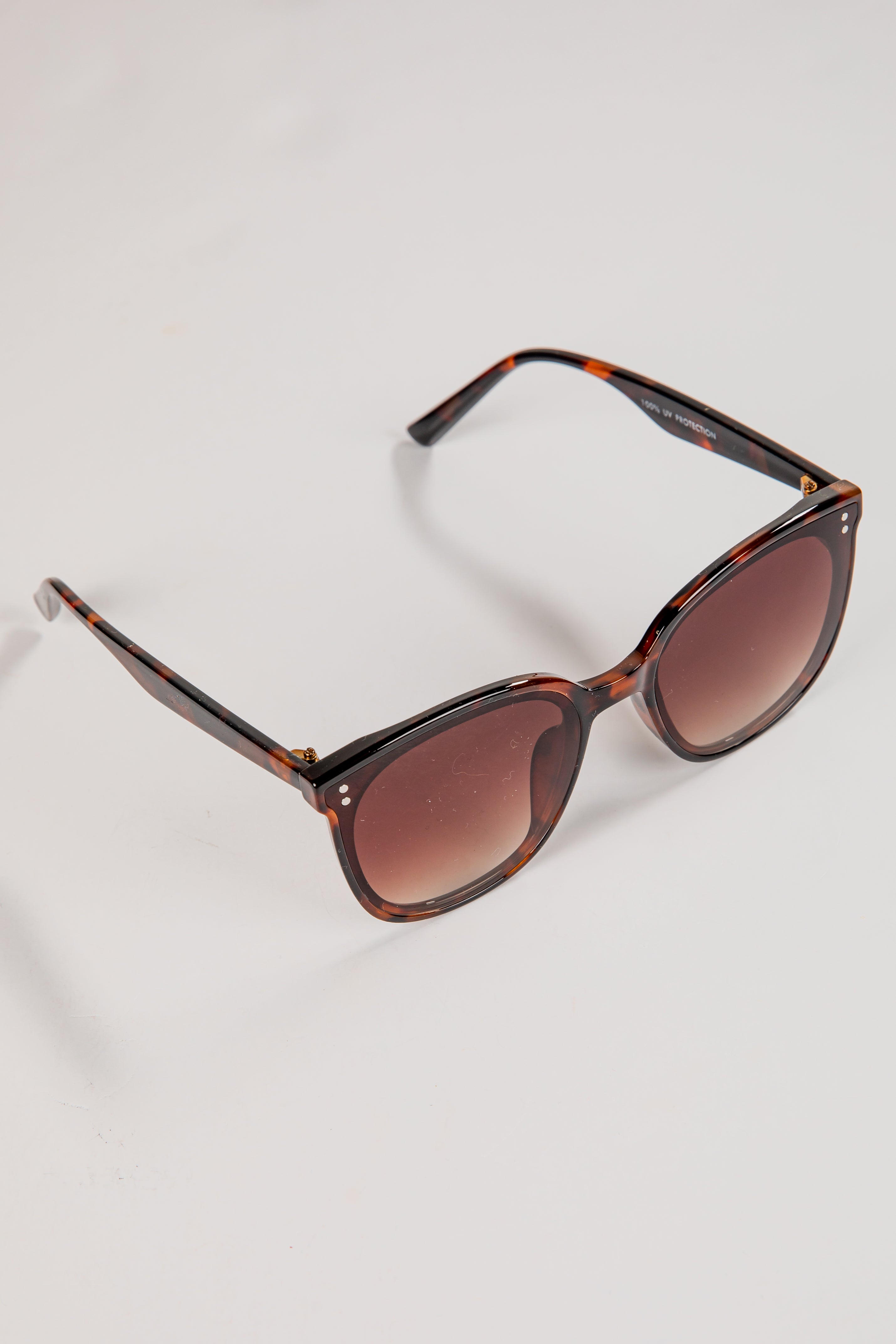 Sunglasses with tortoiseshell frame and brown lenses on a light gray background