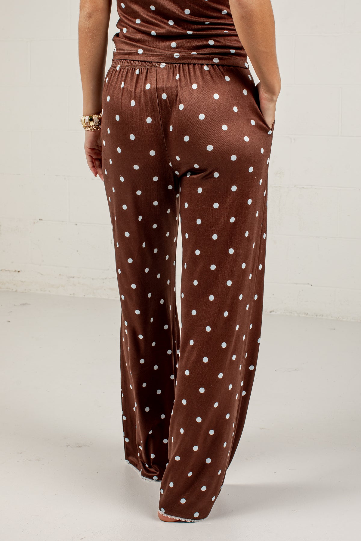 A person shown from the back wearing brown wide-leg pants with a white polka dot pattern, standing against a white wall.