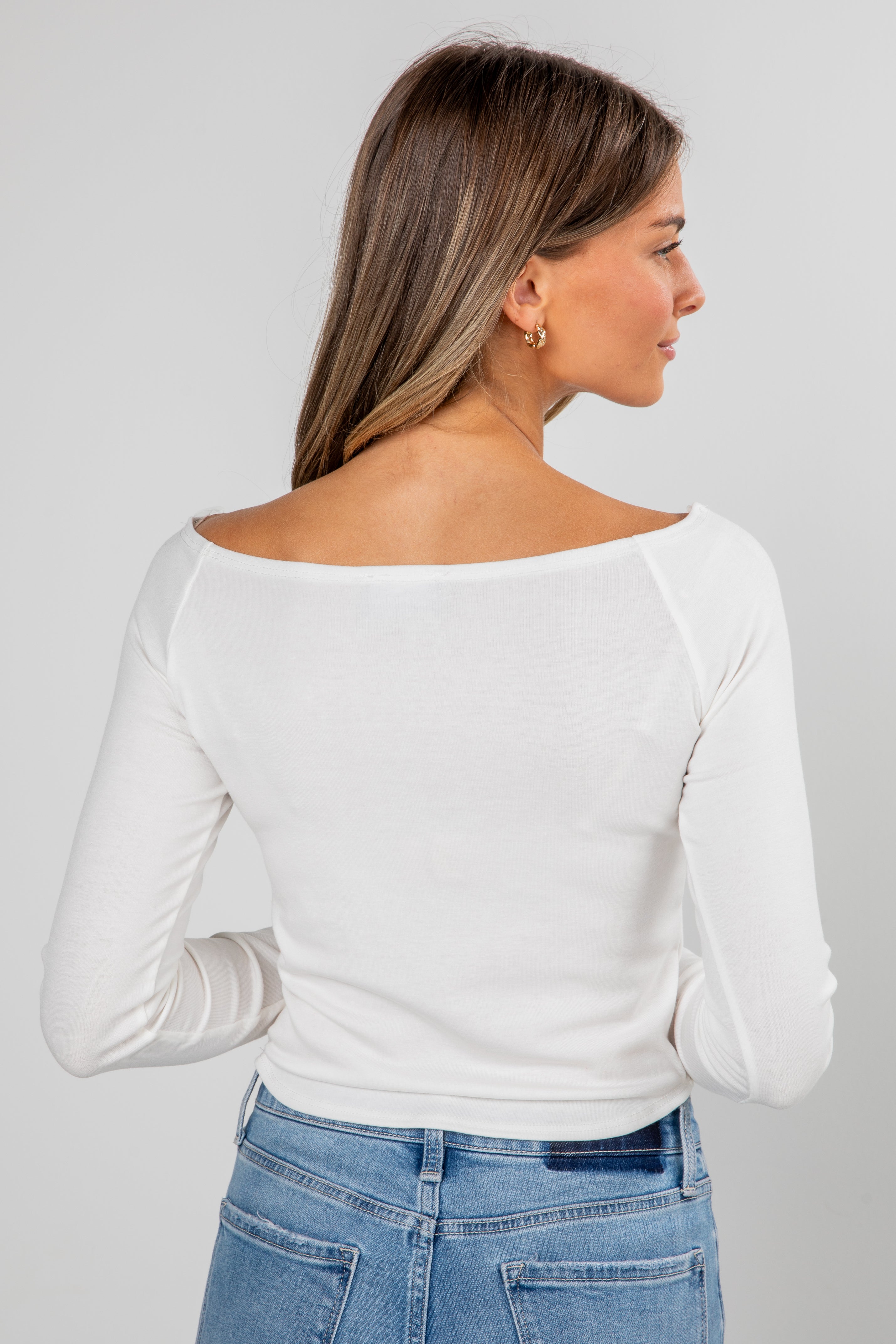 Woman wearing a white long-sleeve top and blue jeans on a plain background
