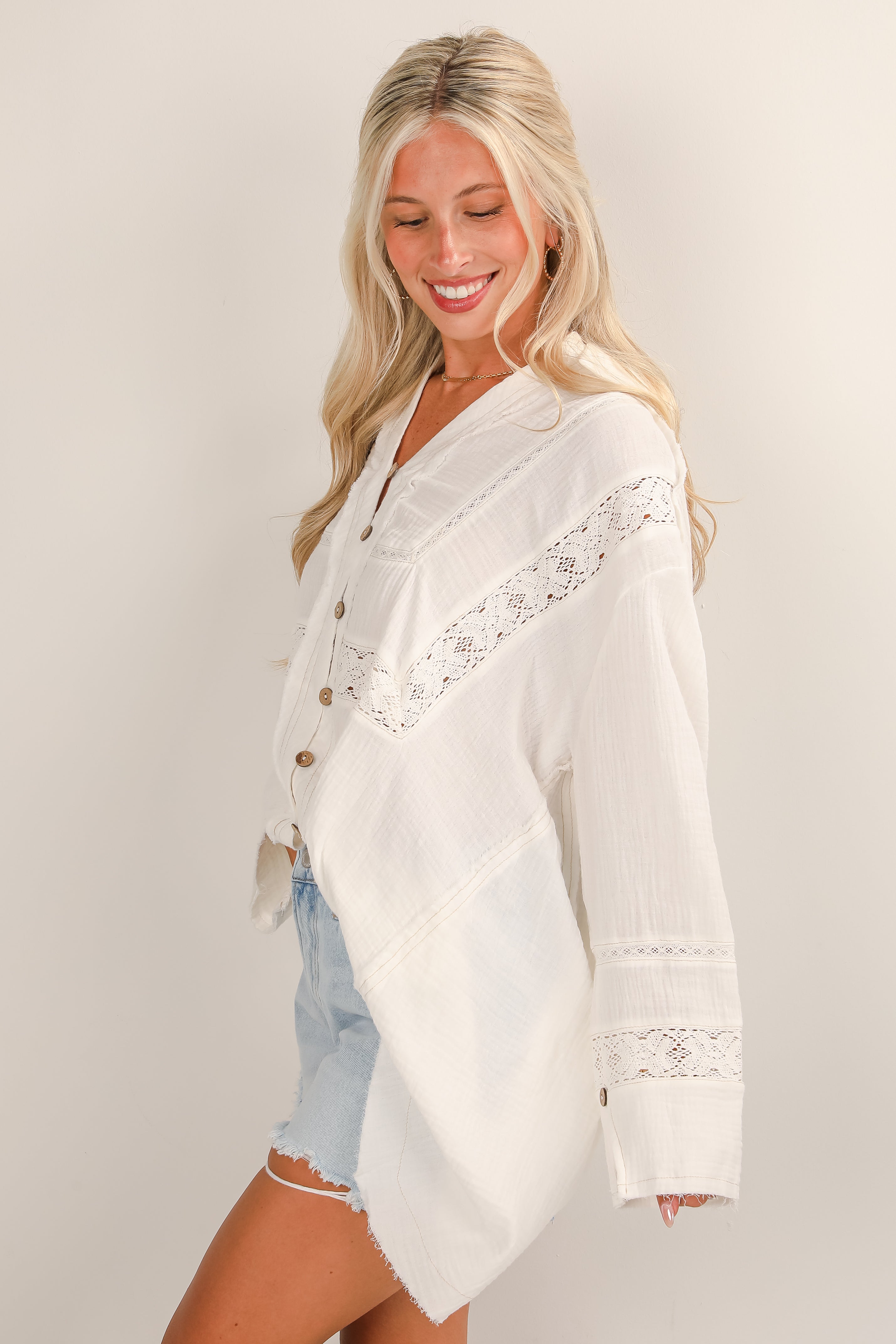 Woman wearing a white lace-trimmed cardigan over a light blue top against a plain background