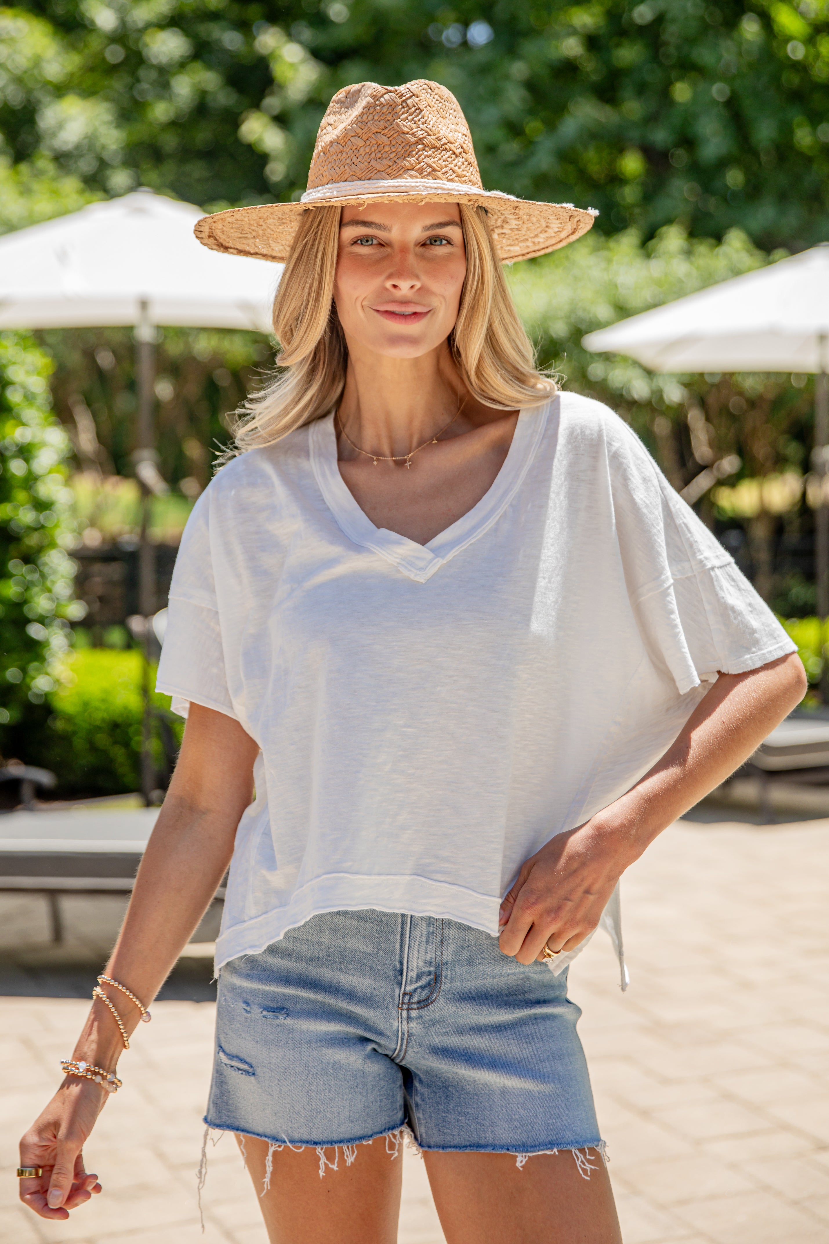 Woman wearing a straw hat, white shirt, and blue jeans outdoors.