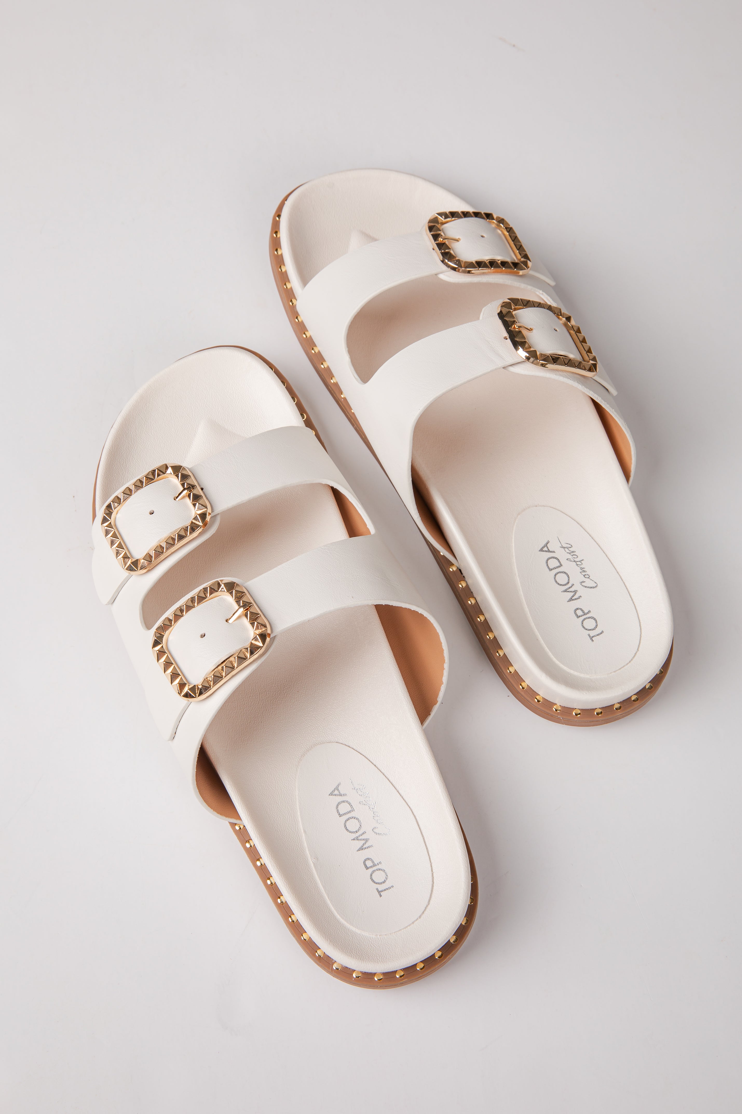 Pair of white sandals with gold buckles on a light gray background