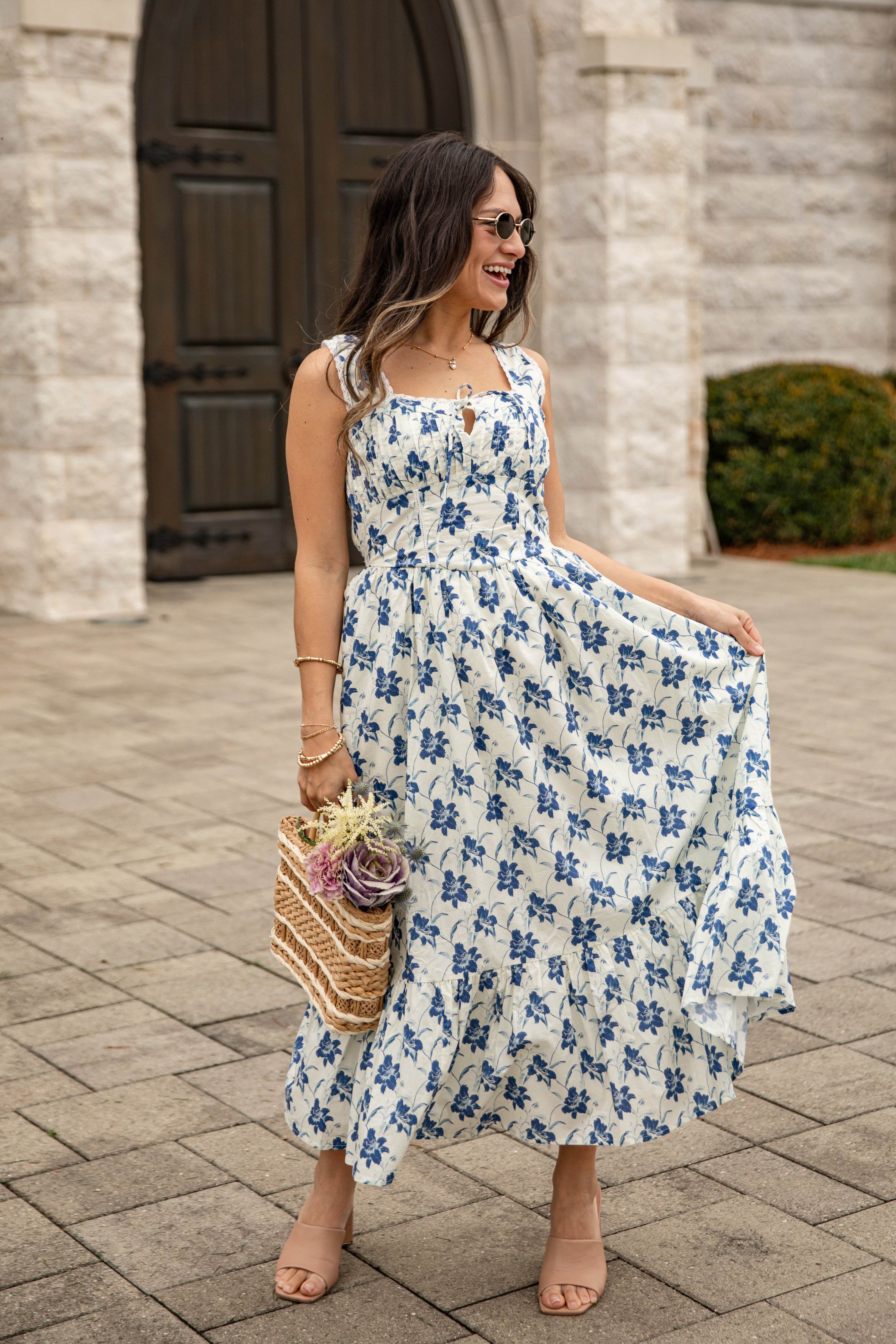 Woman in a floral dress standing on a stone pathway with a building in the background