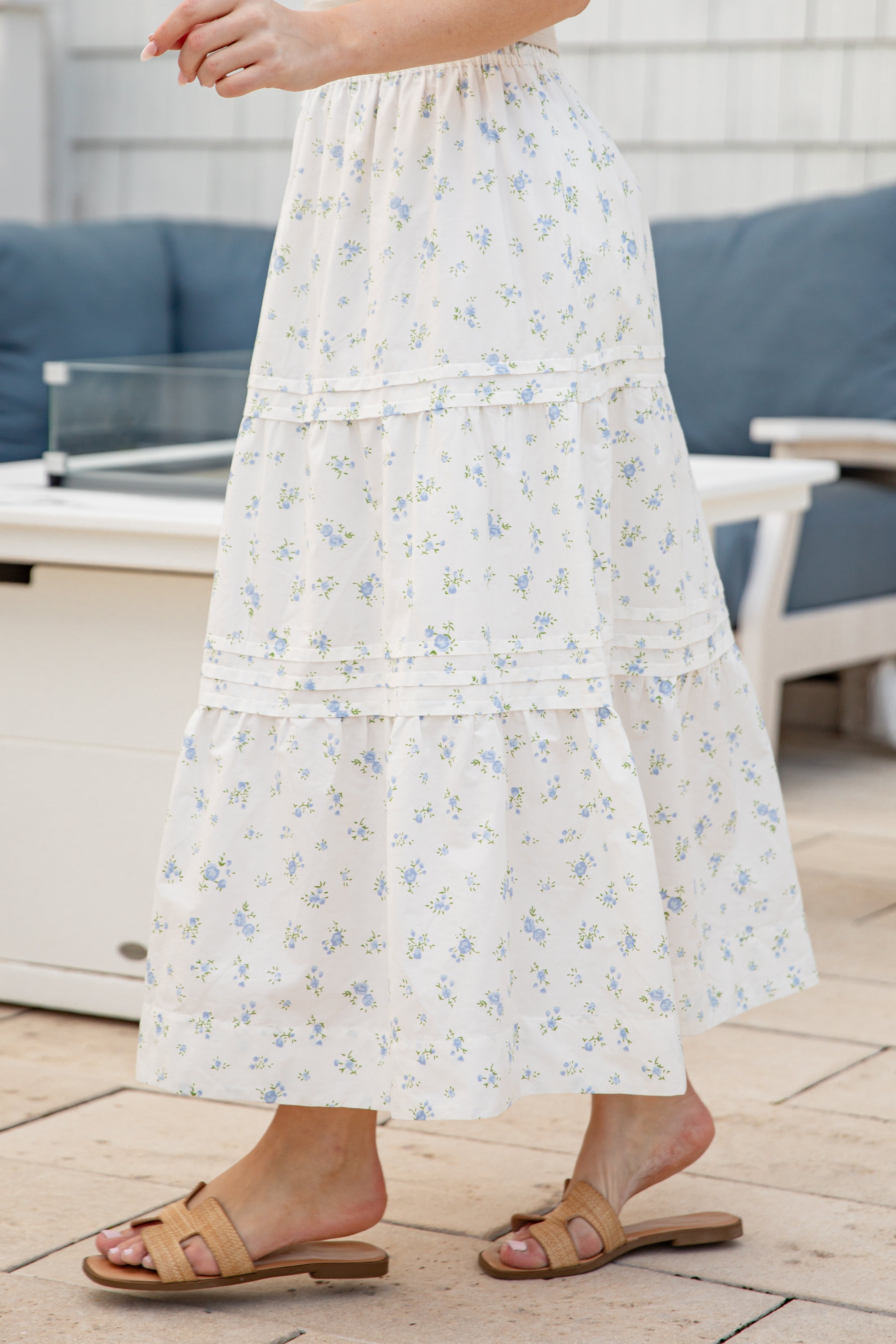 Person wearing a white floral dress standing on a wooden deck.