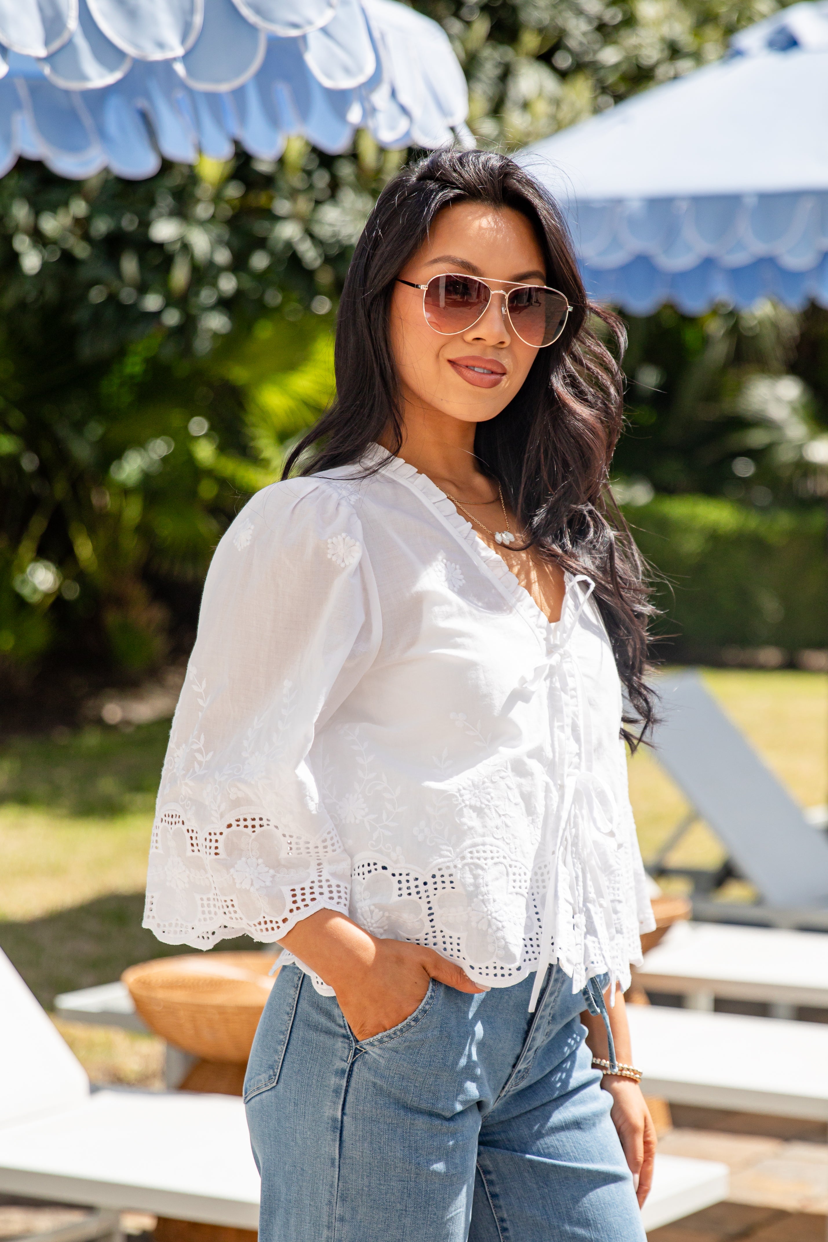 Woman wearing a white blouse and sunglasses outdoors with greenery in the background