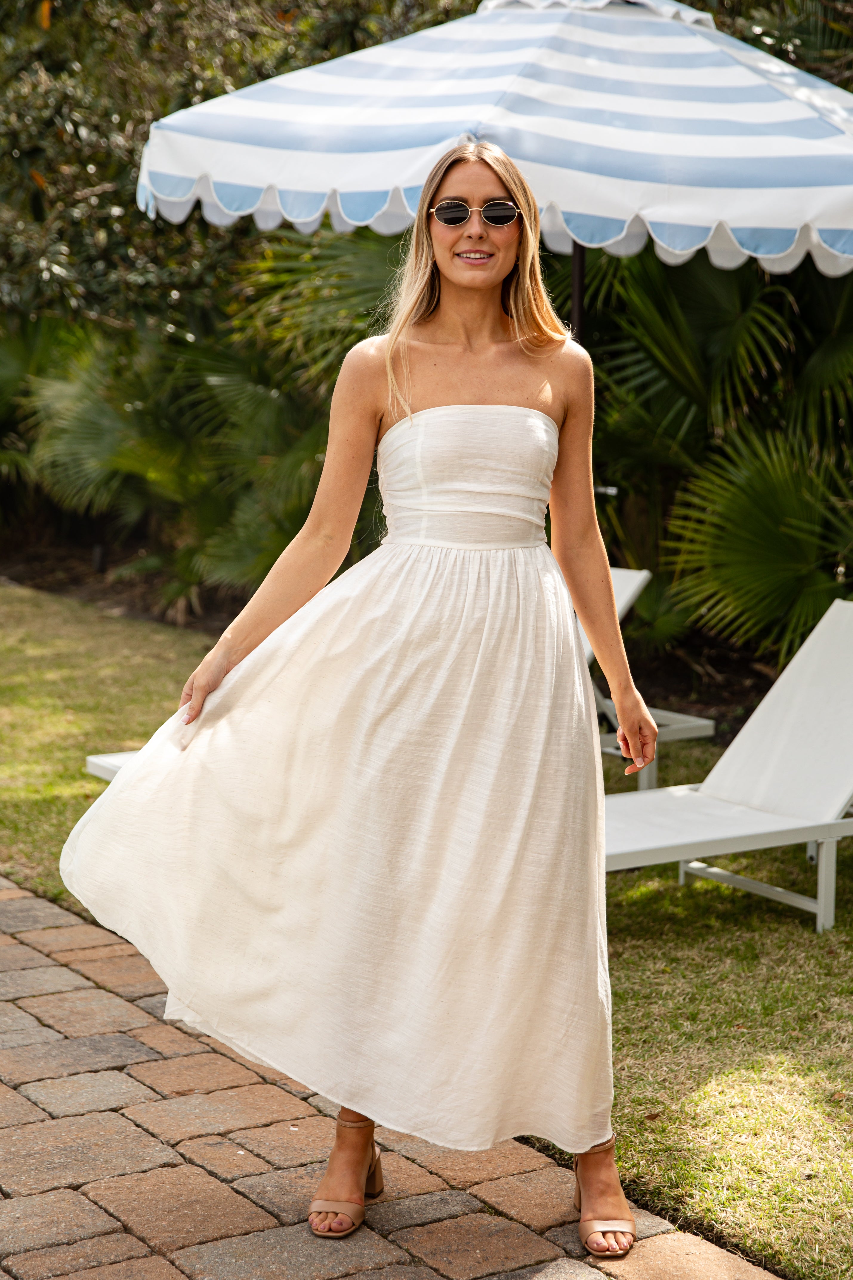 Woman in a white dress standing under a striped umbrella in a garden setting