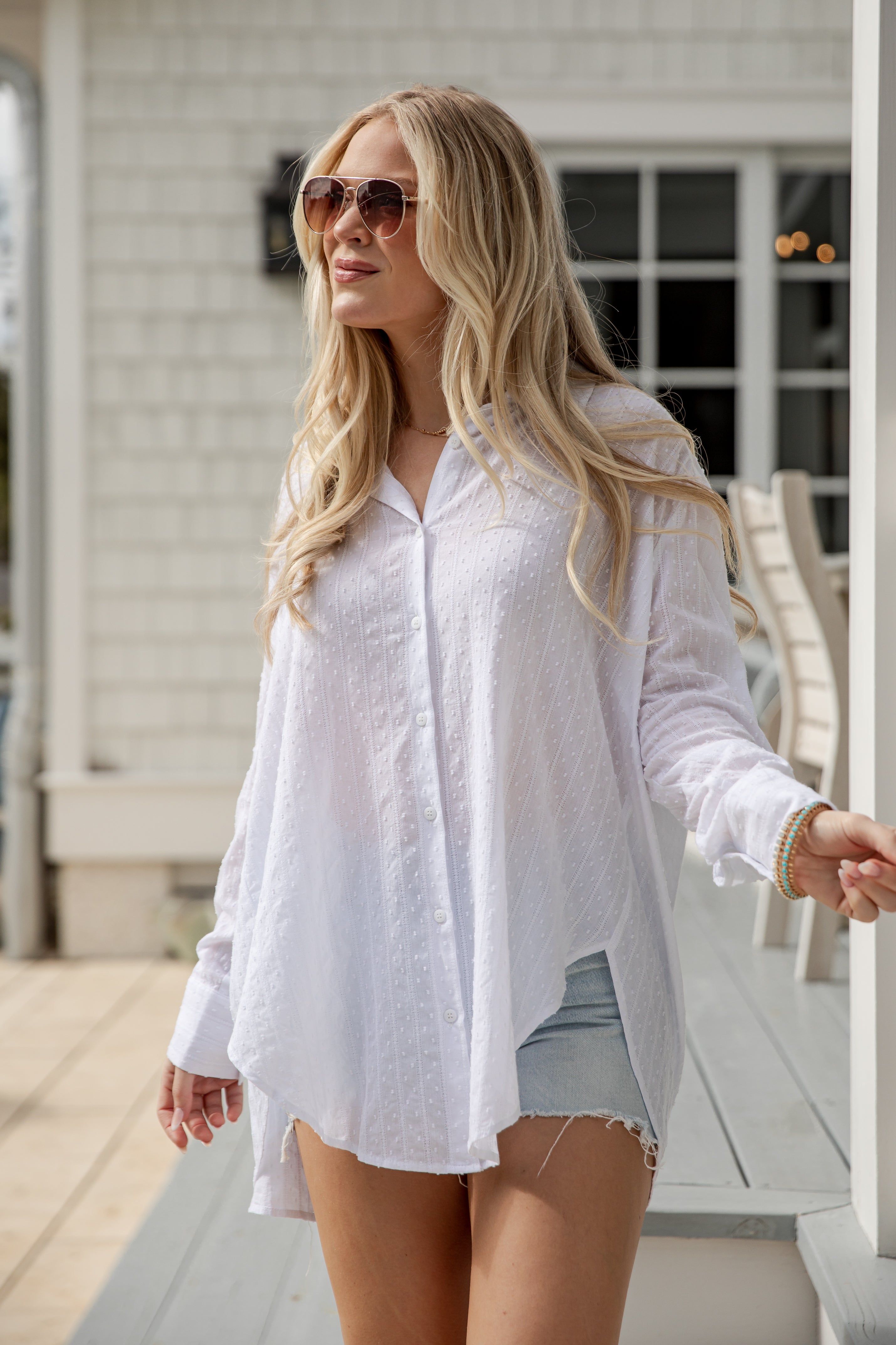 Woman wearing a white shirt and denim shorts on a porch.