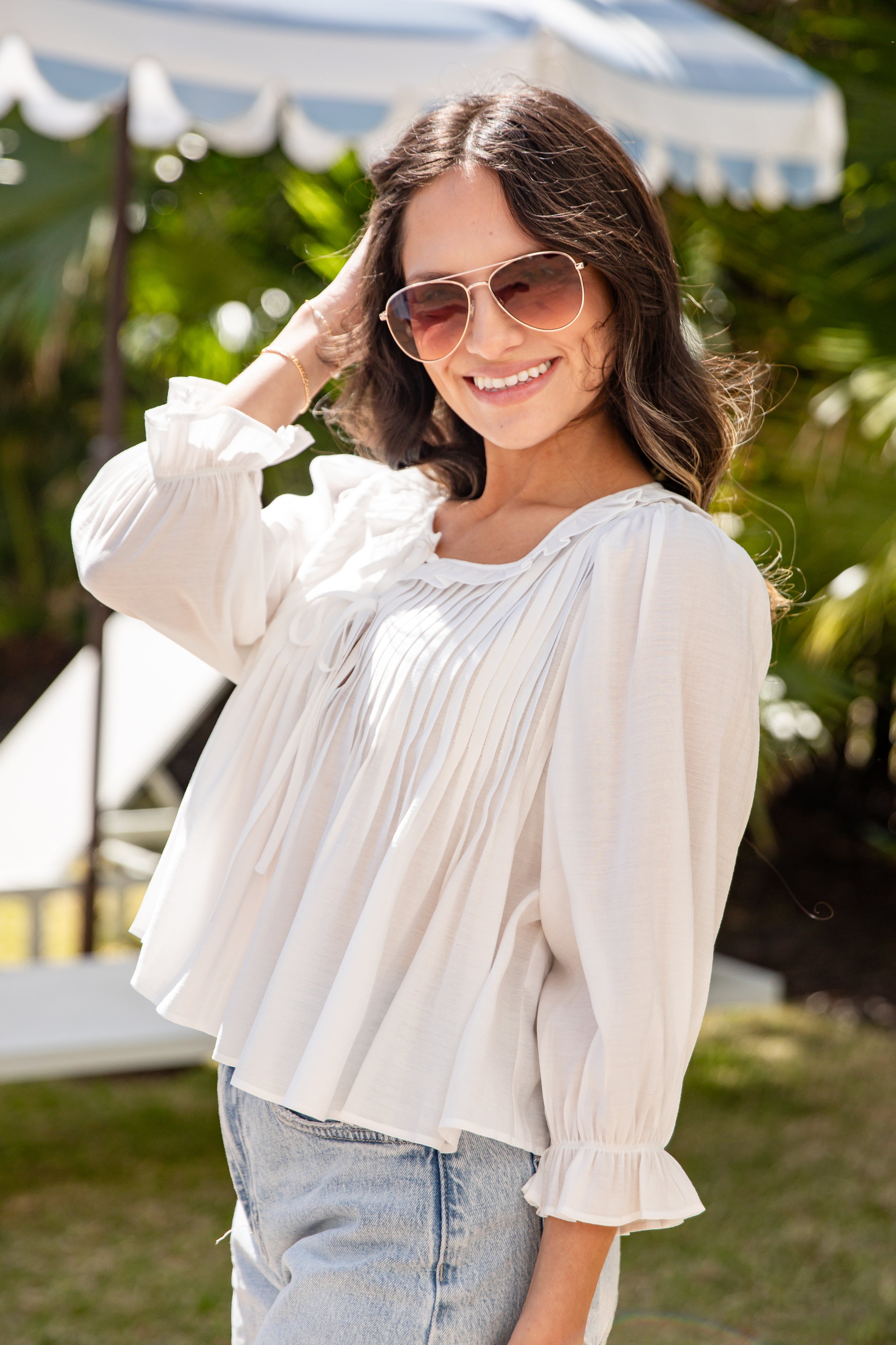 Woman wearing a white blouse and sunglasses outdoors with greenery in the background