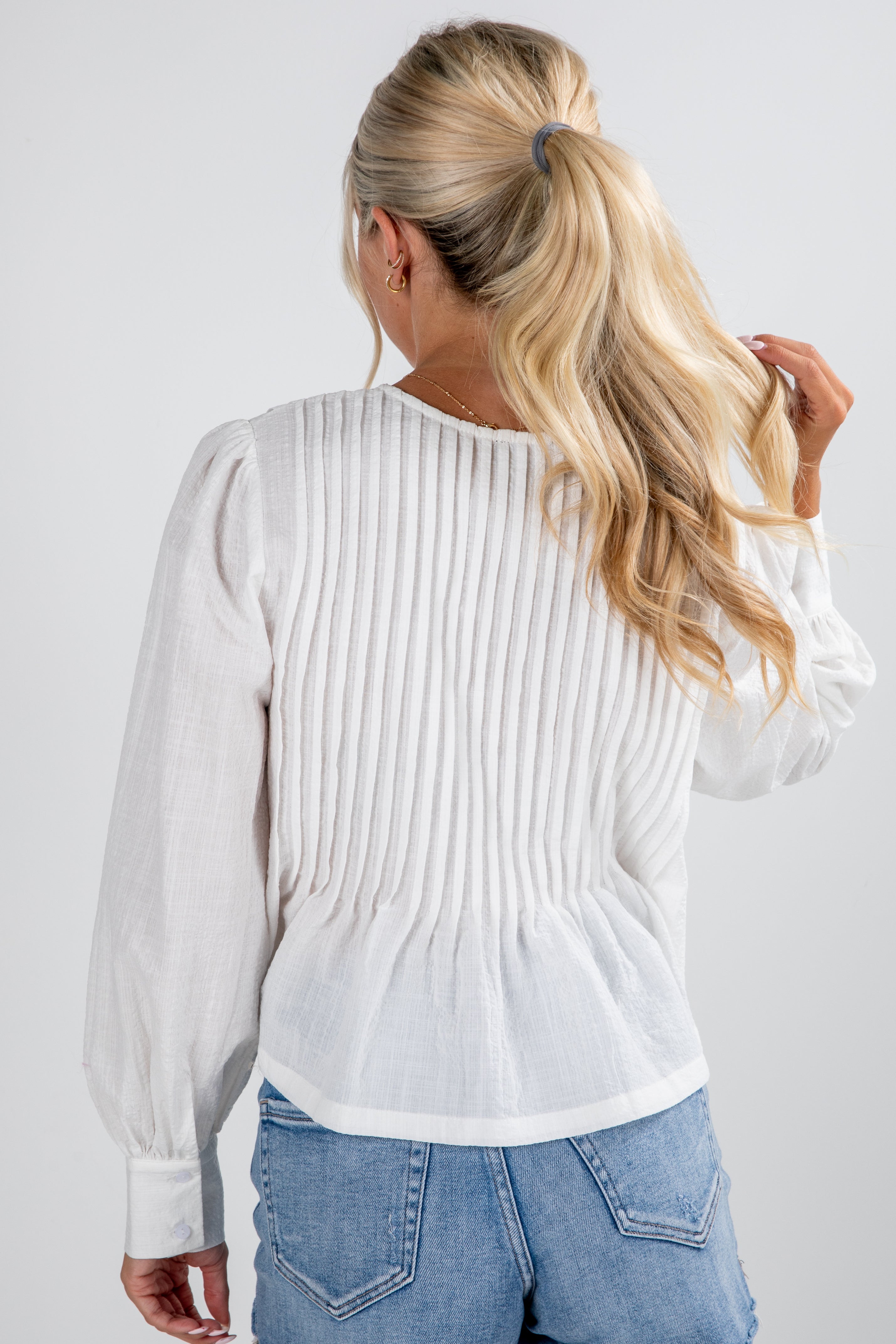 Woman wearing a white ribbed sweater and blue jeans on a plain background
