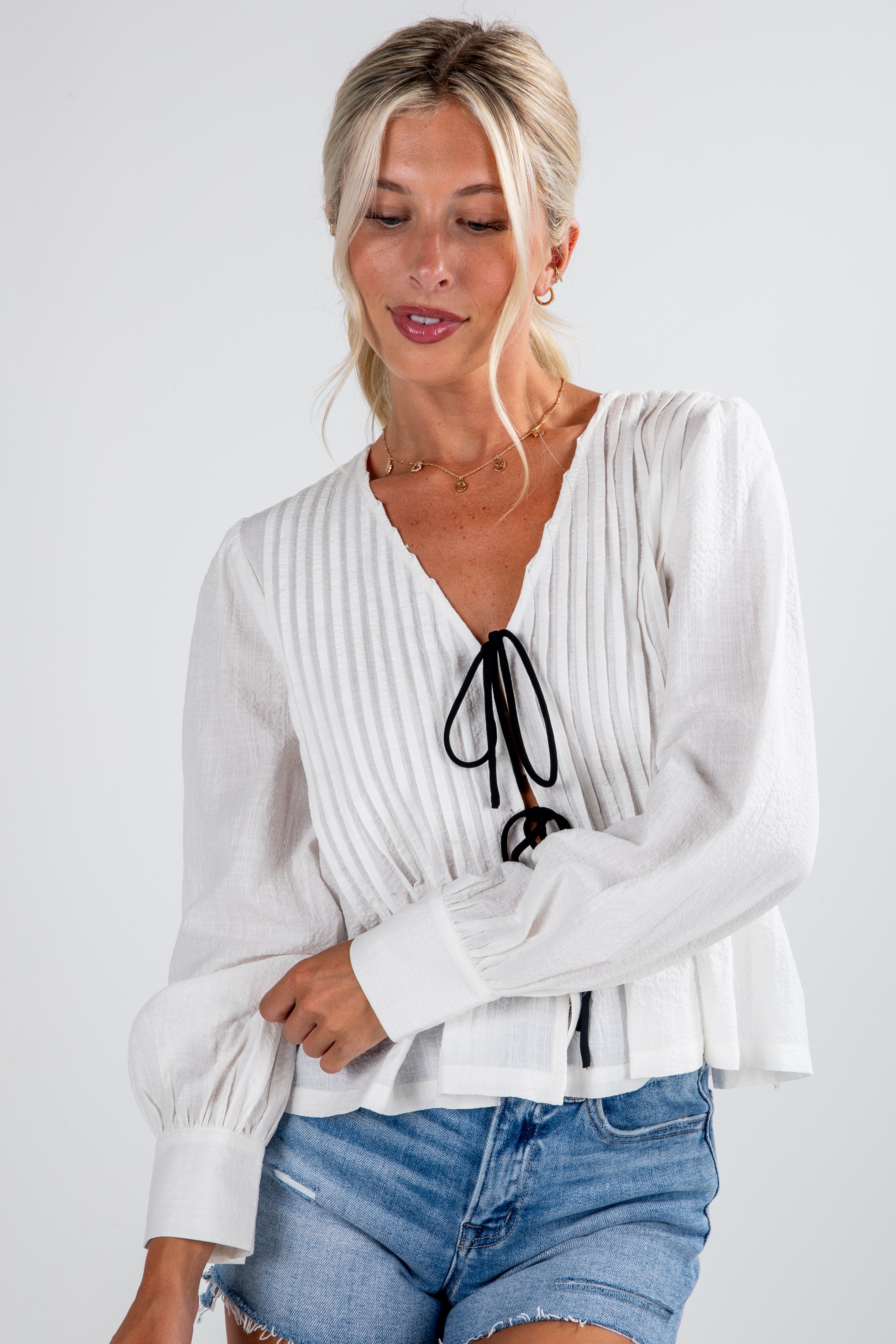 Woman wearing a white blouse with long sleeves and blue shorts on a plain background