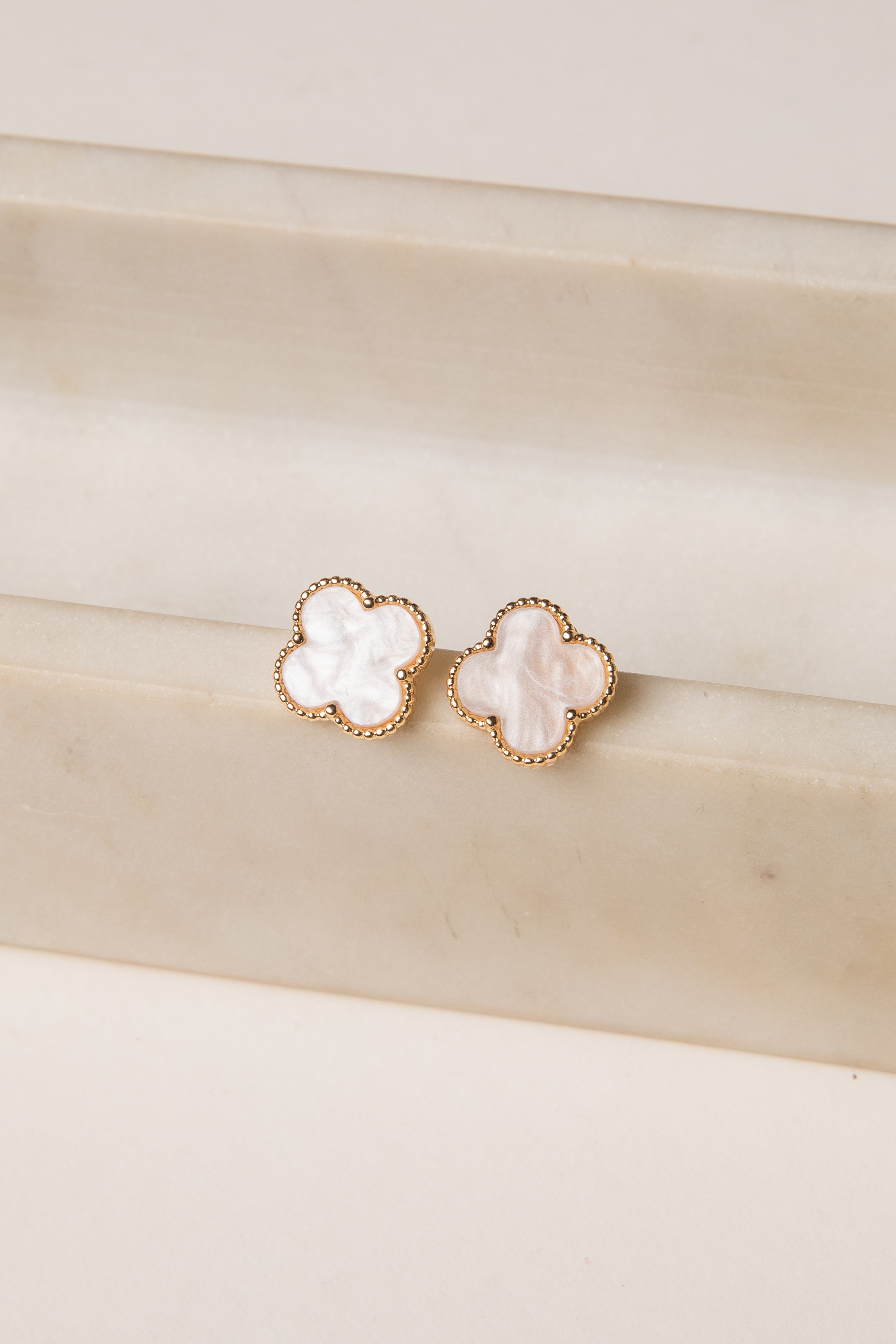 Pair of gold earrings with white stones on a beige surface