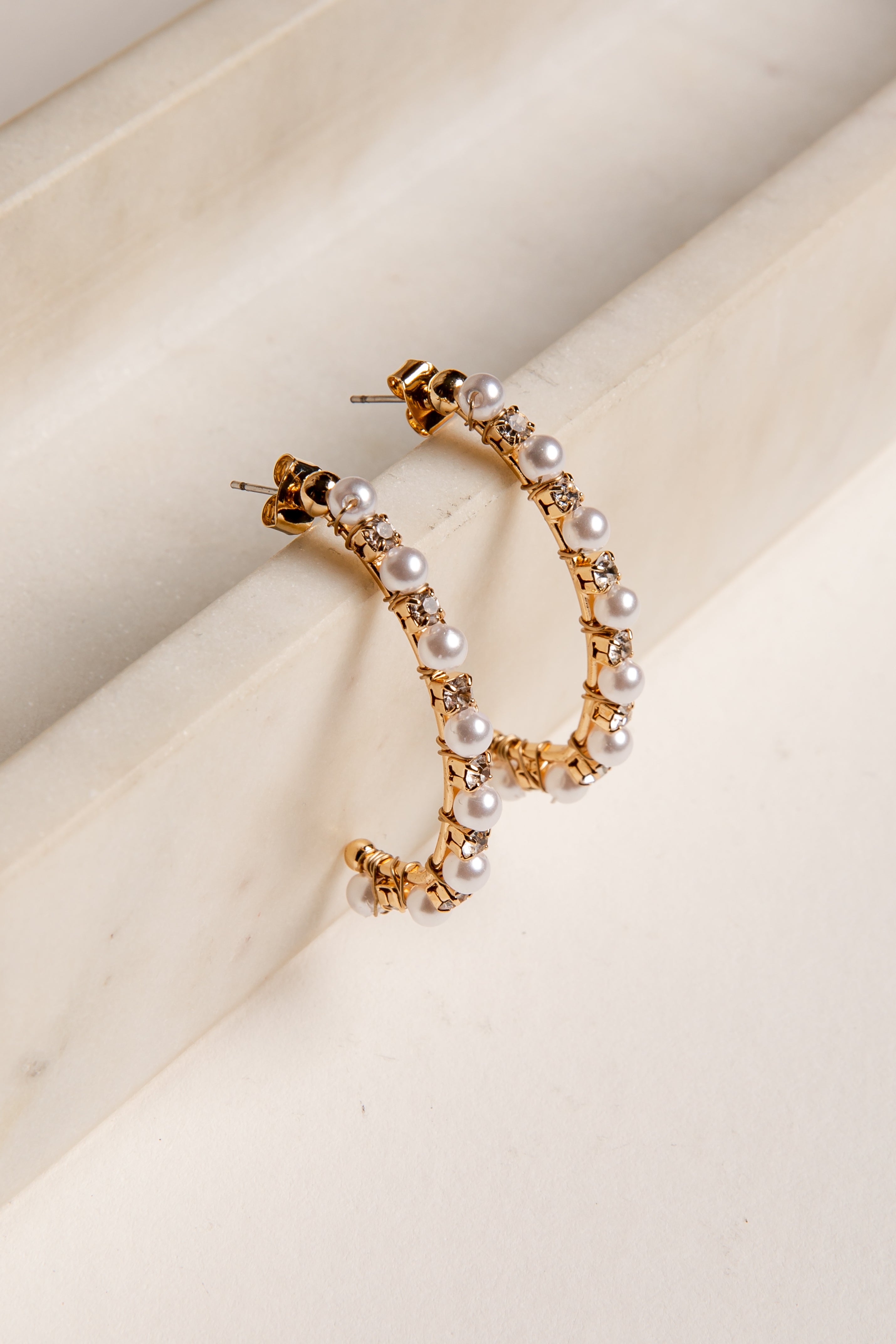 Gold hoop earrings with pearls on a beige surface