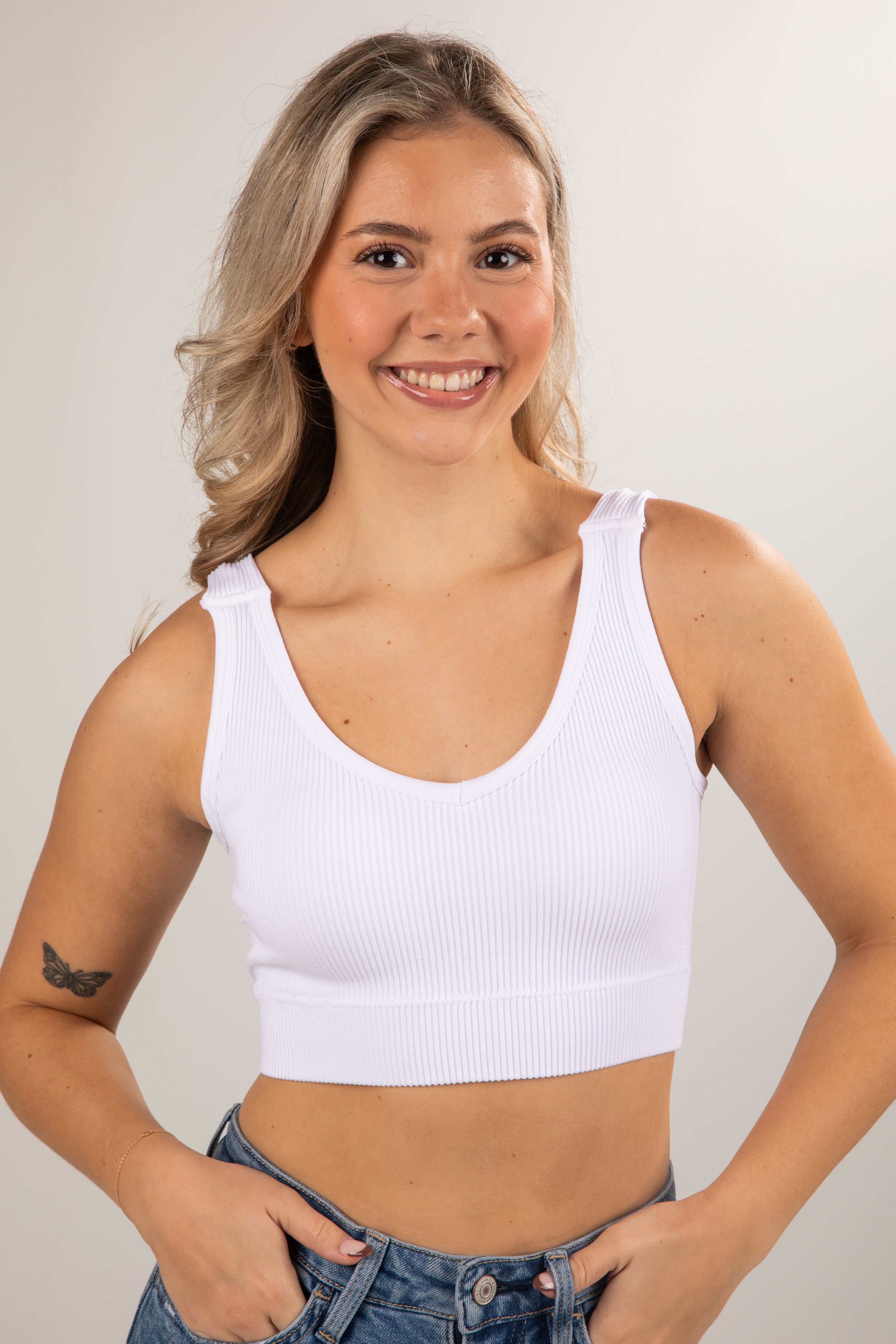 Woman wearing a white tank top against a plain background