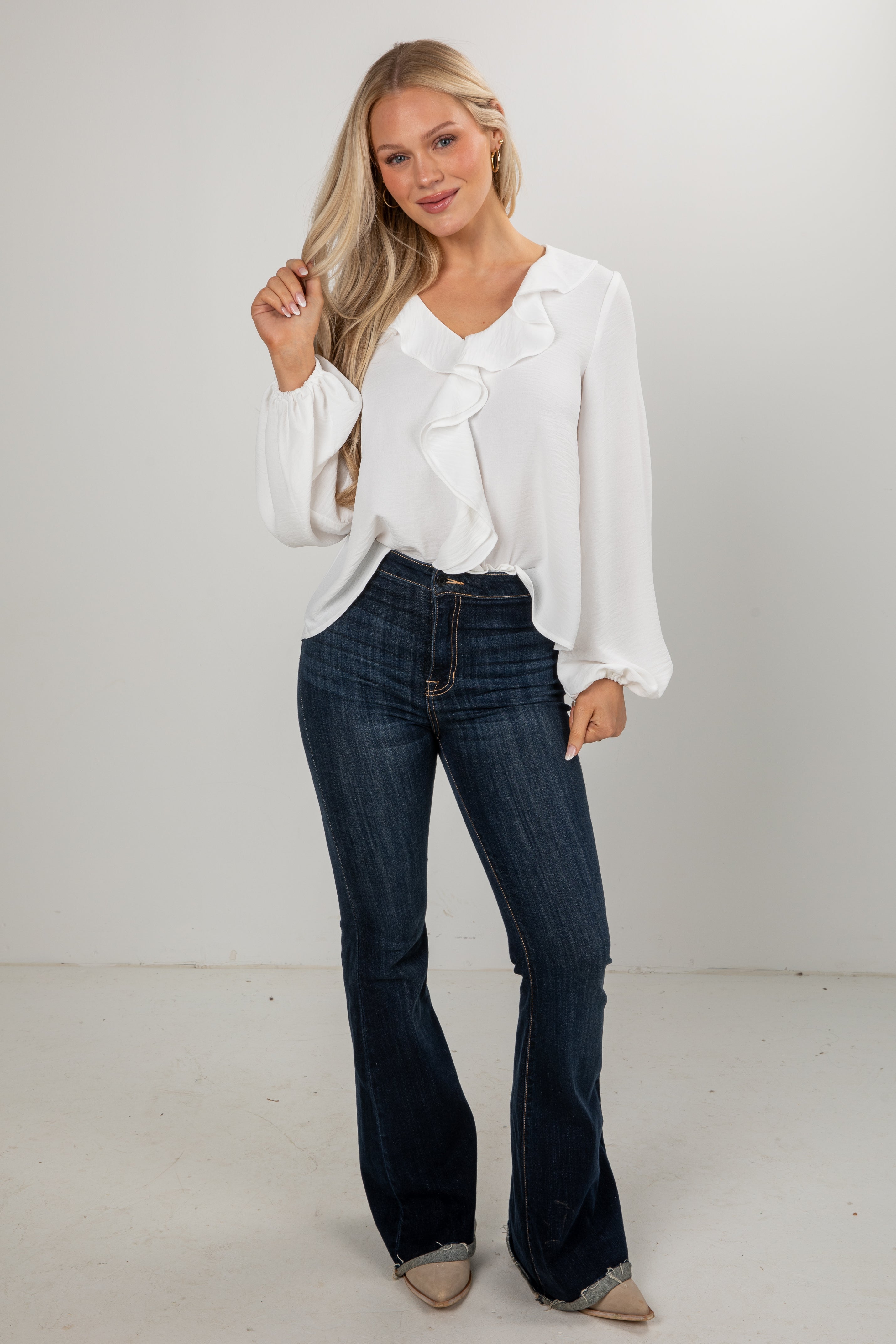 Woman wearing a white blouse and dark jeans against a plain background