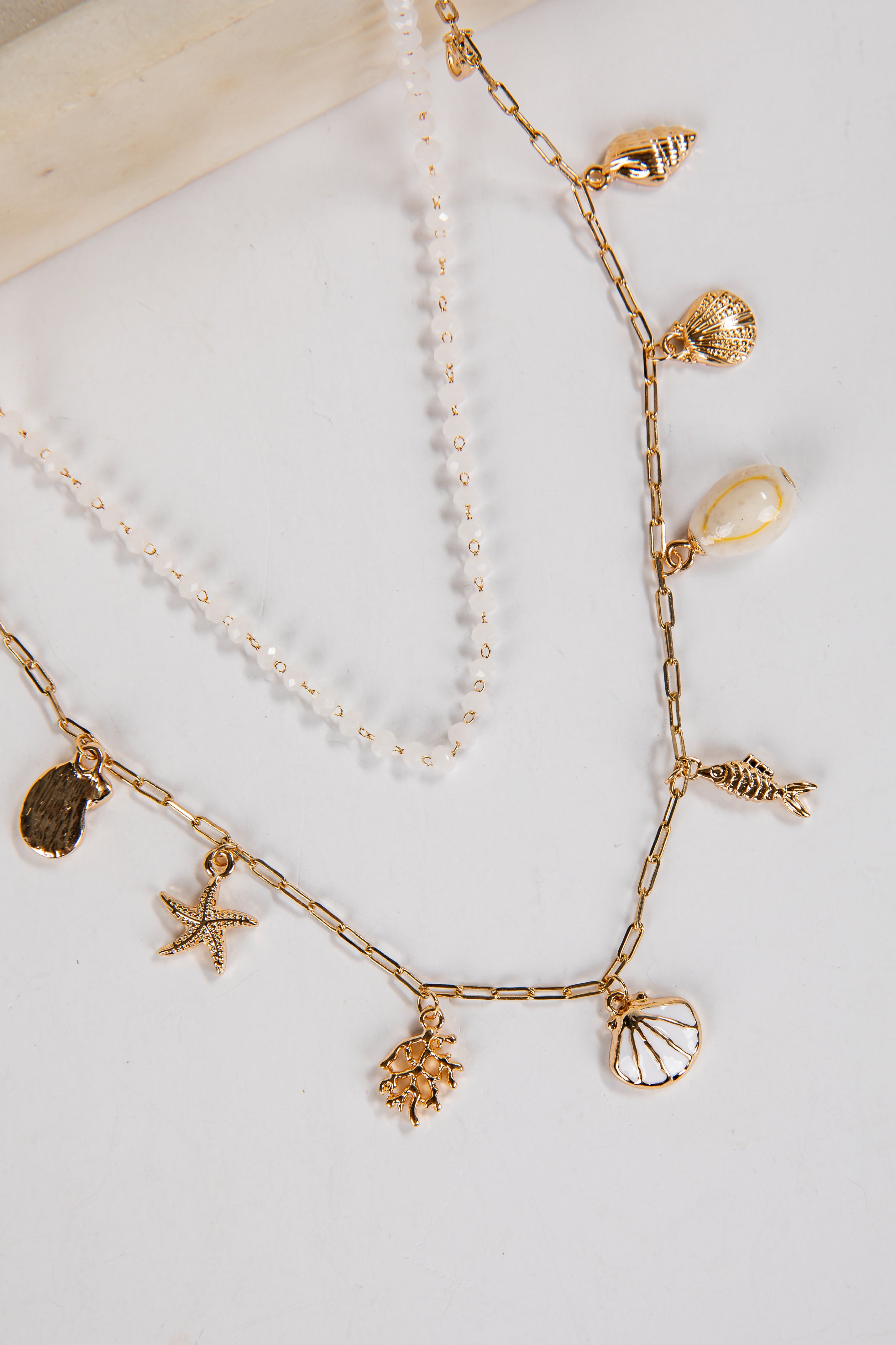 Gold necklace with shell and starfish charms on a white background
