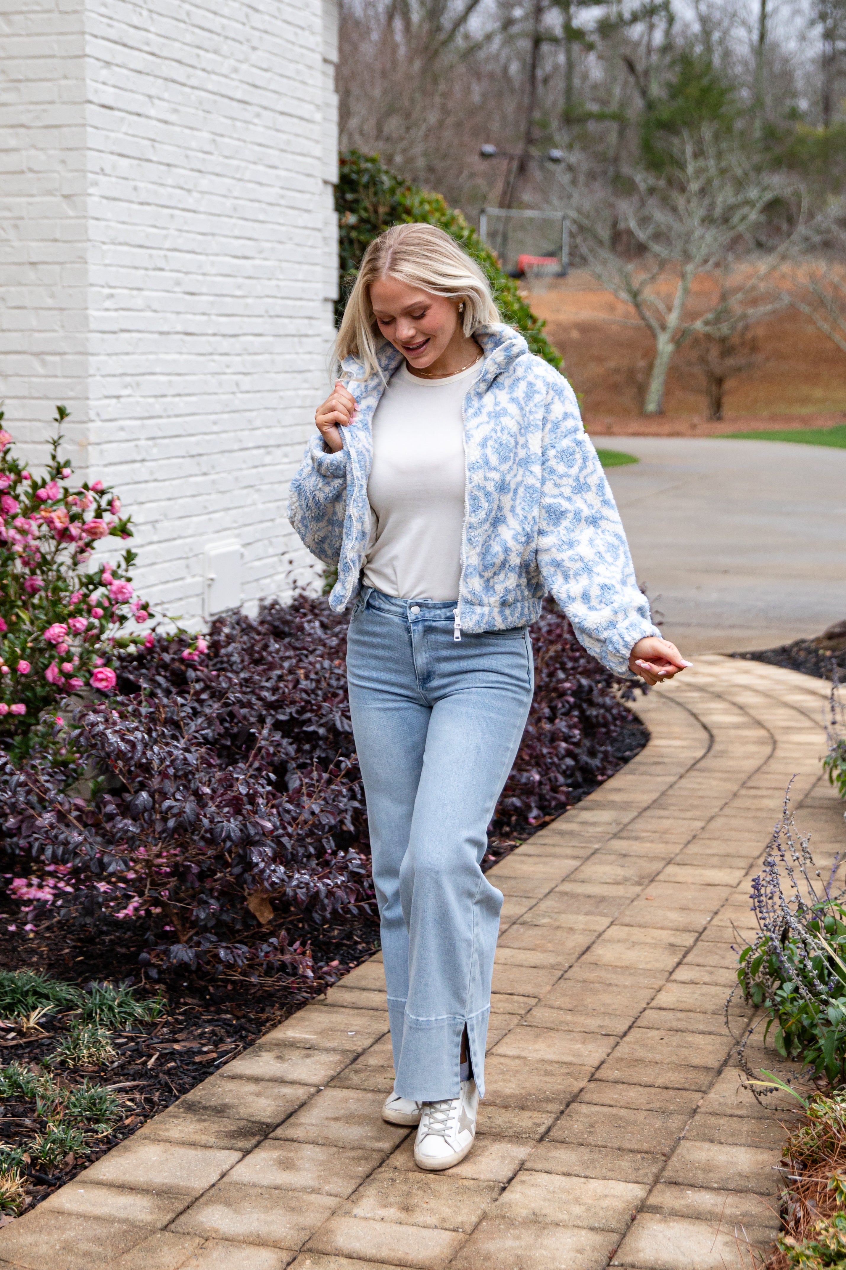 Woman walking on a brick path with flowers and a building in the background