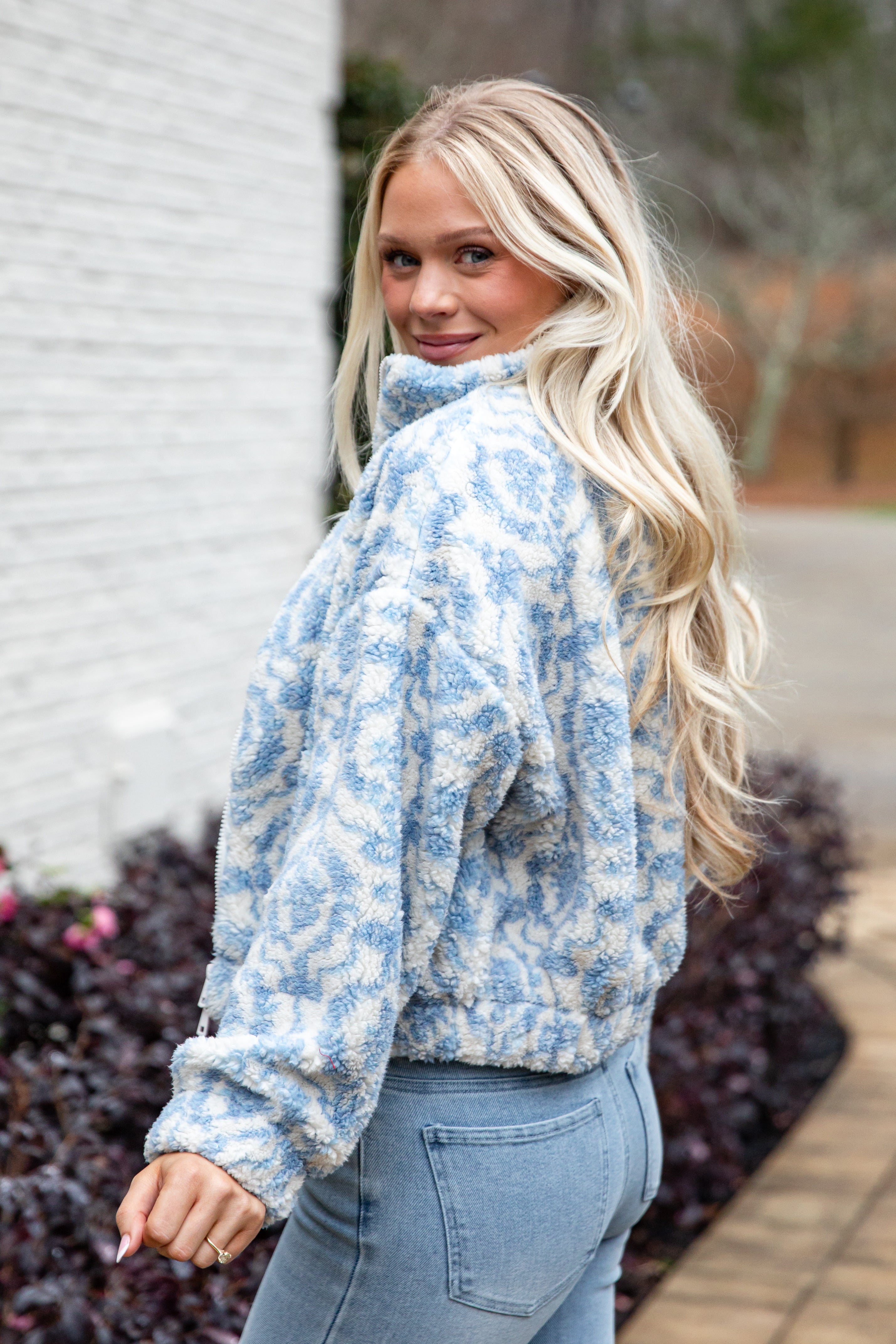Woman wearing a blue floral jacket and jeans standing outdoors.