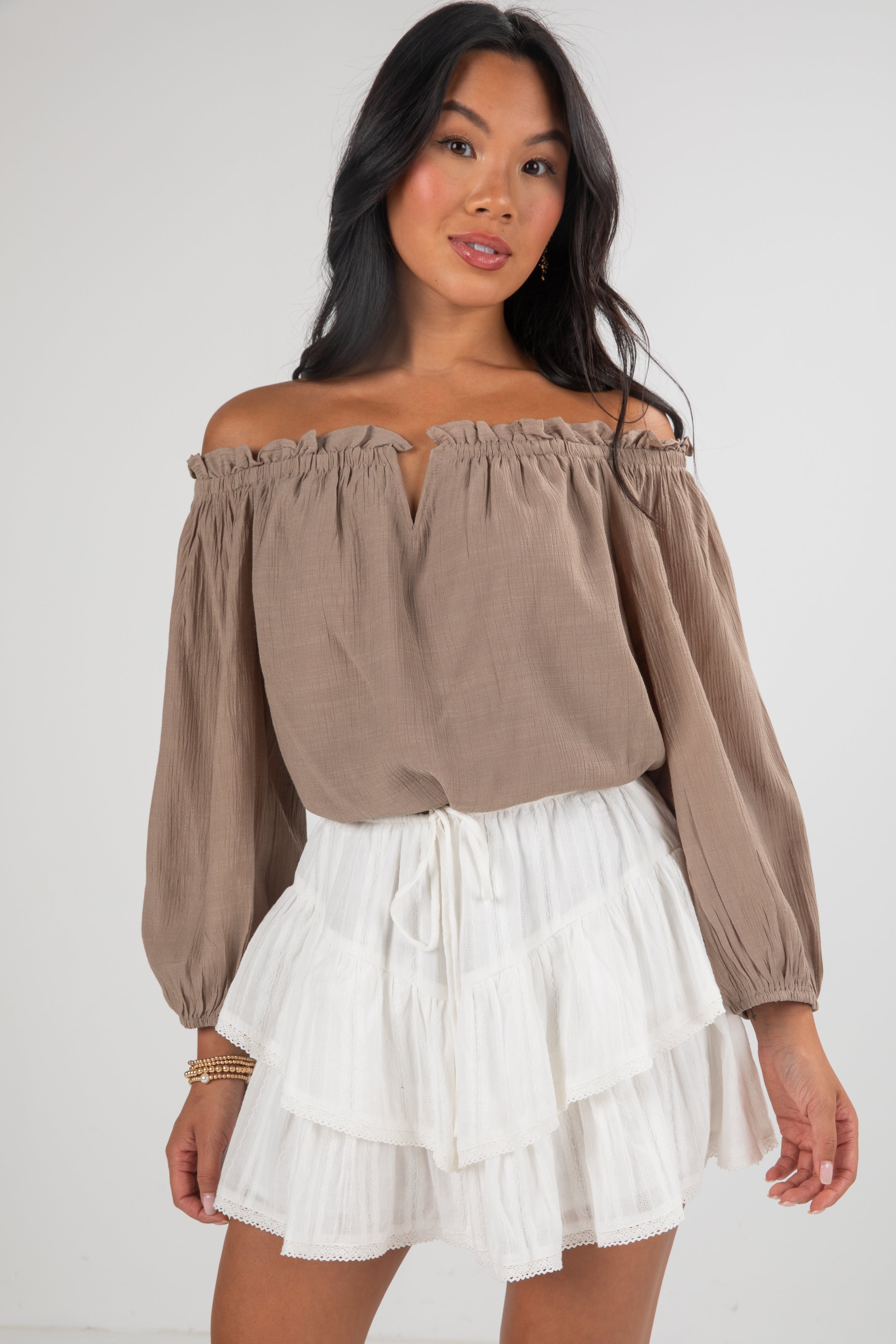Woman wearing a brown off-shoulder top and white skirt on a white background