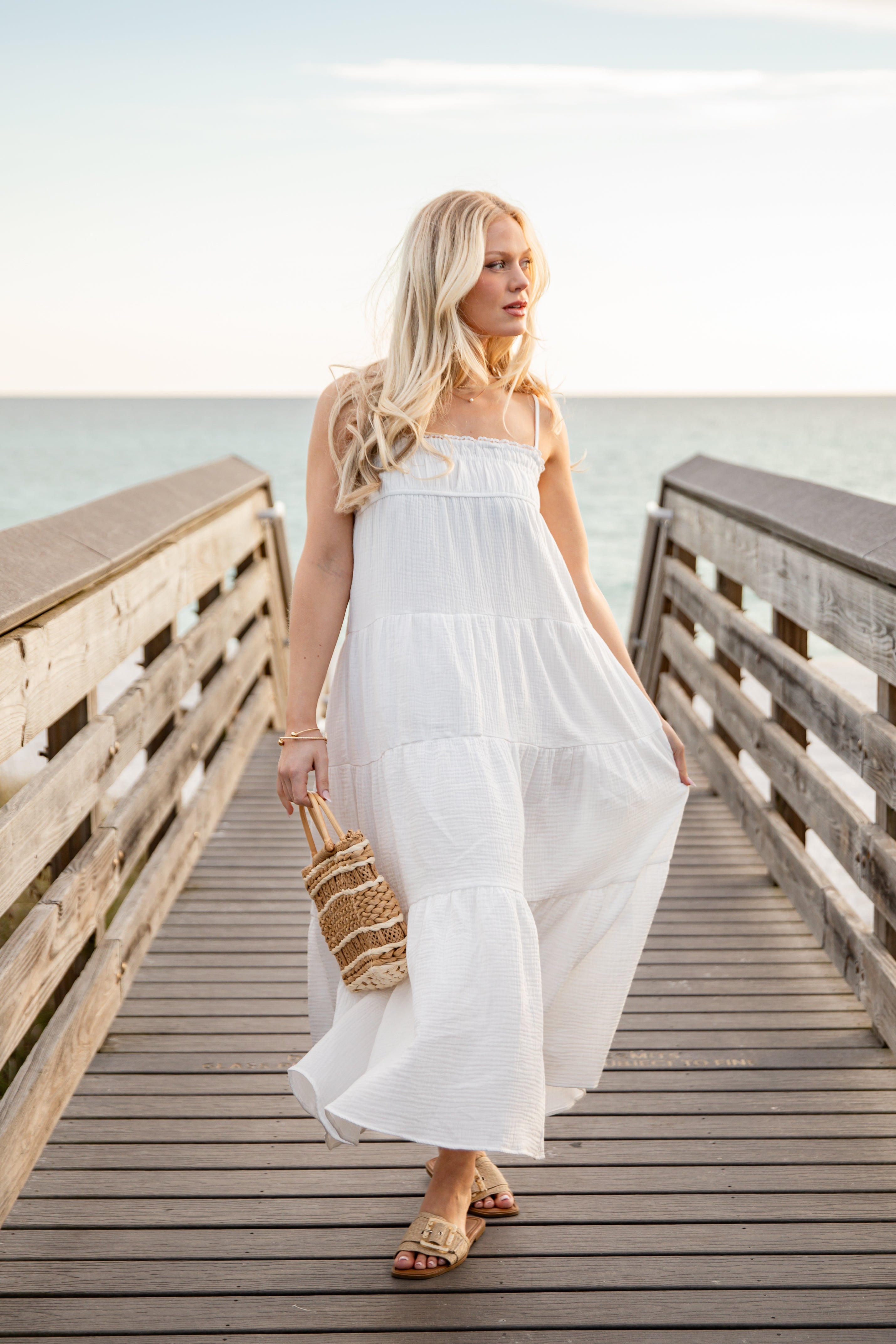 Woman in a white dress standing on a wooden pier by the water