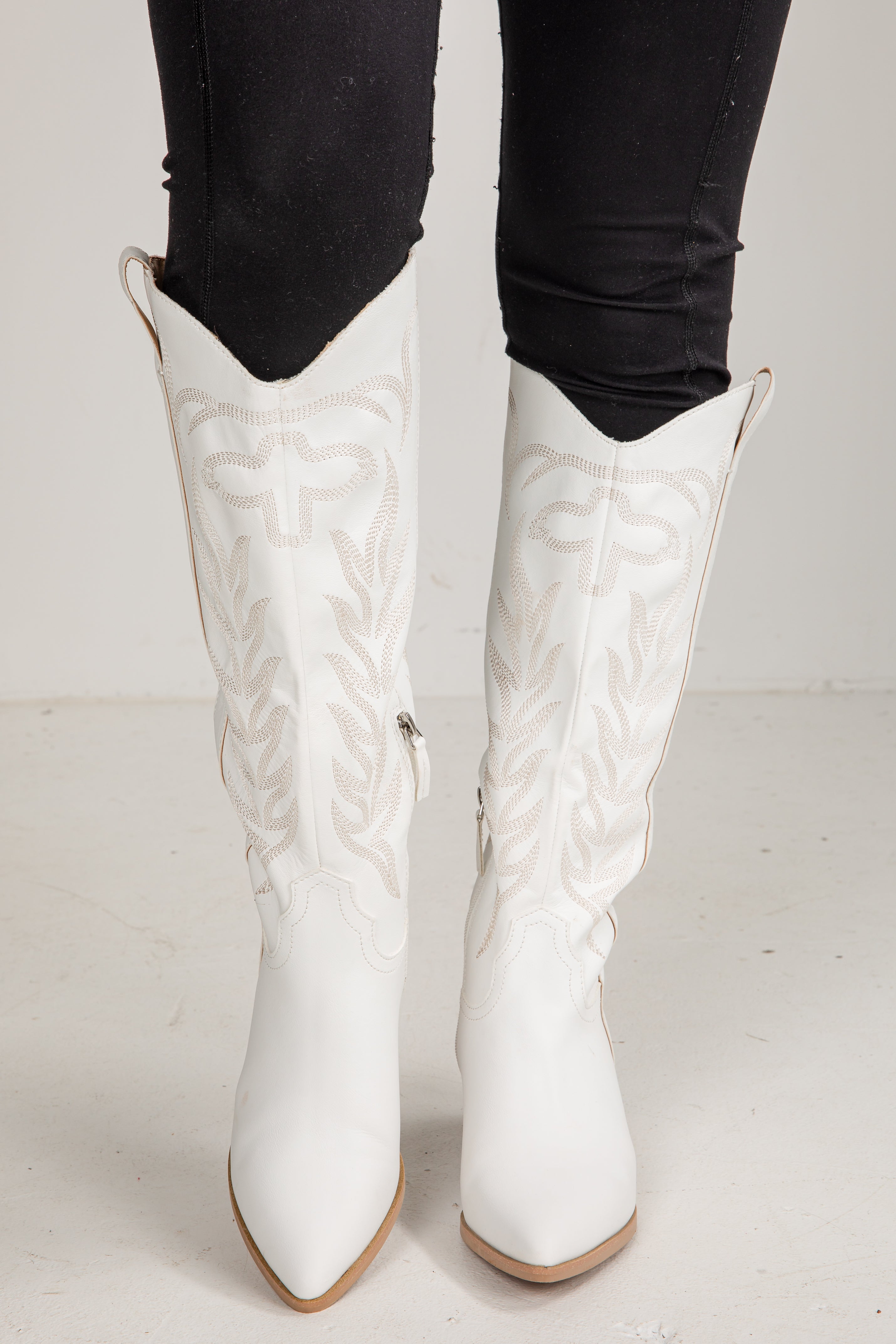White knee-high boots with black pants on a light background