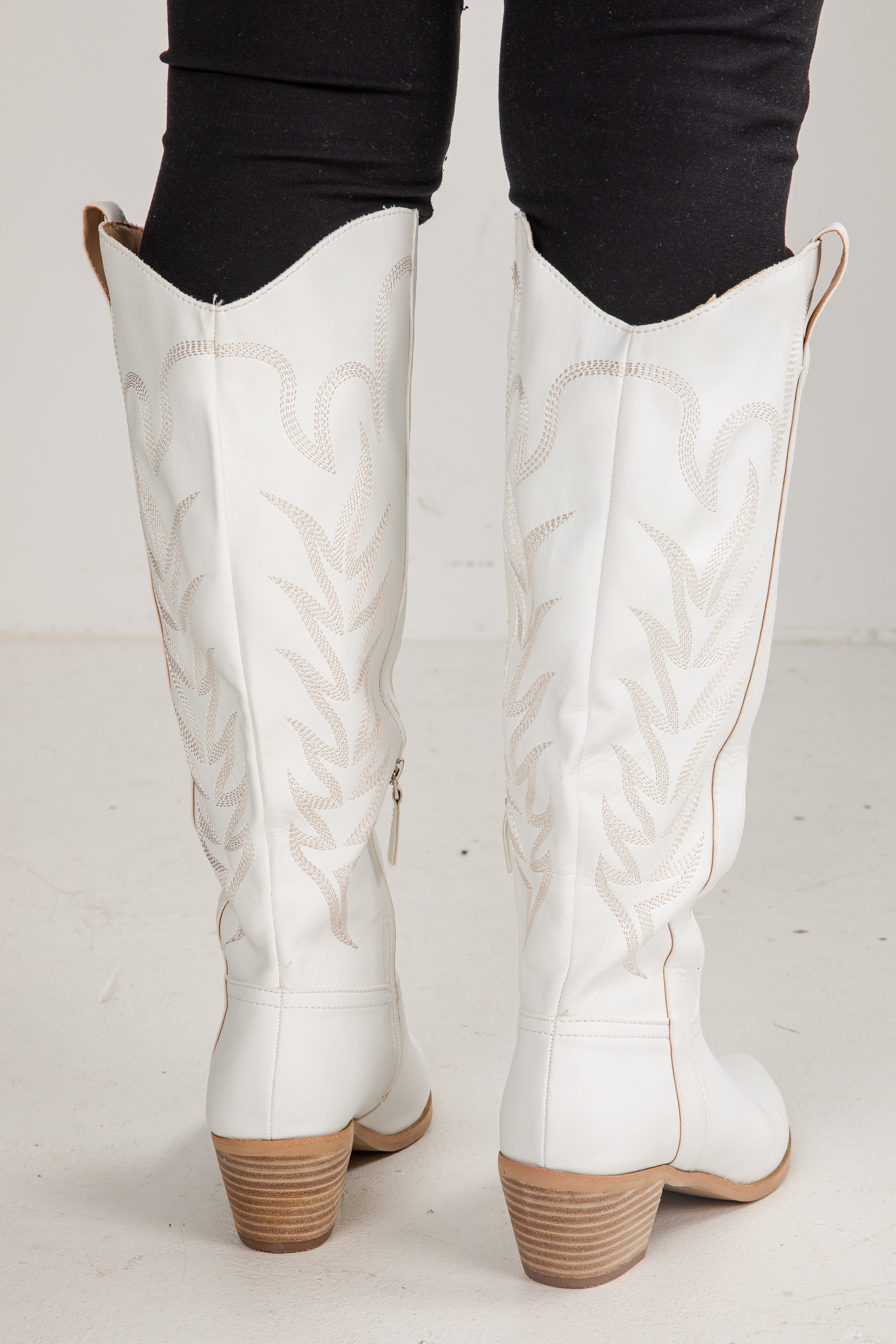 White knee-high boots with brown soles worn by a person on a light gray background
