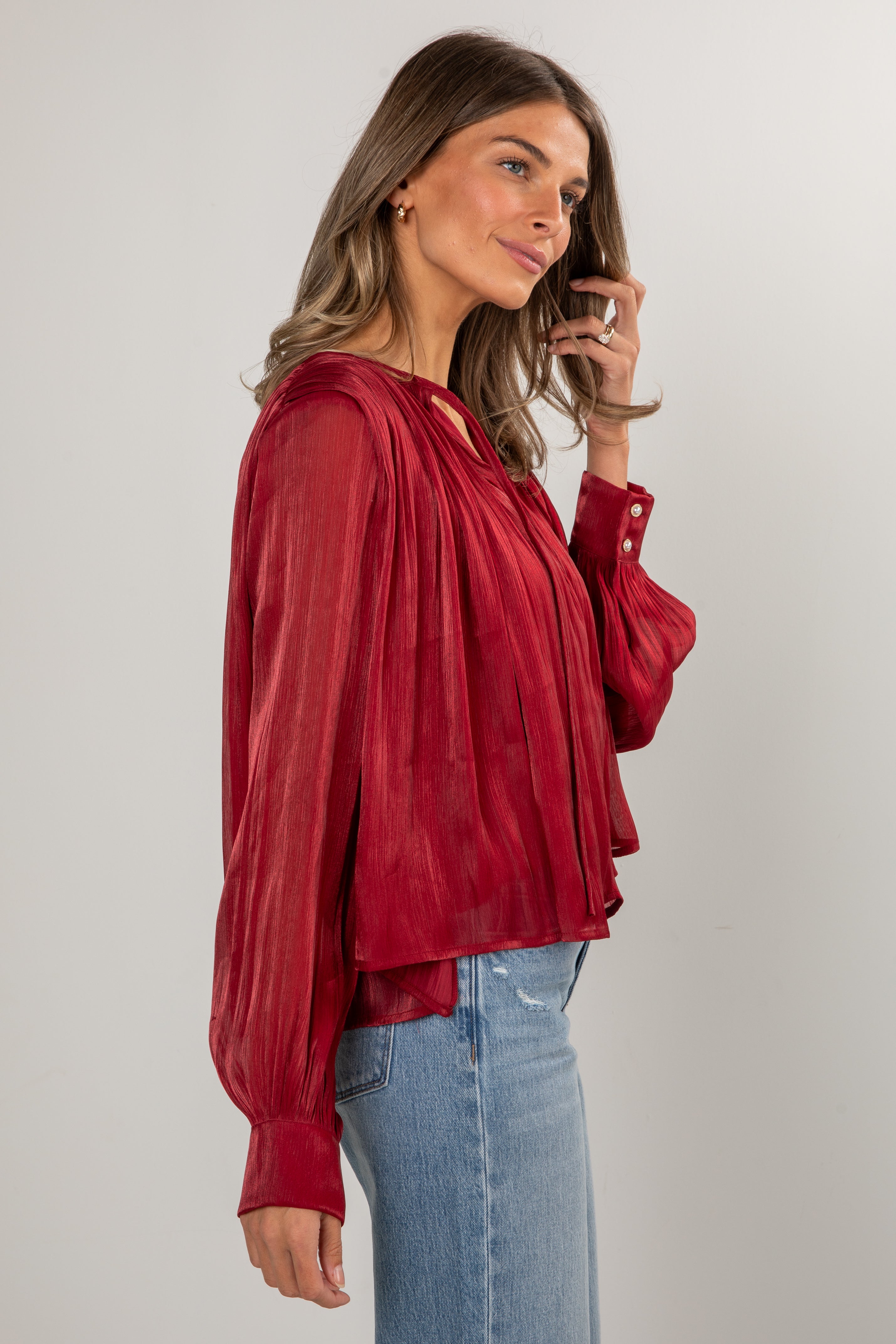 Woman wearing a red blouse and blue jeans against a plain background